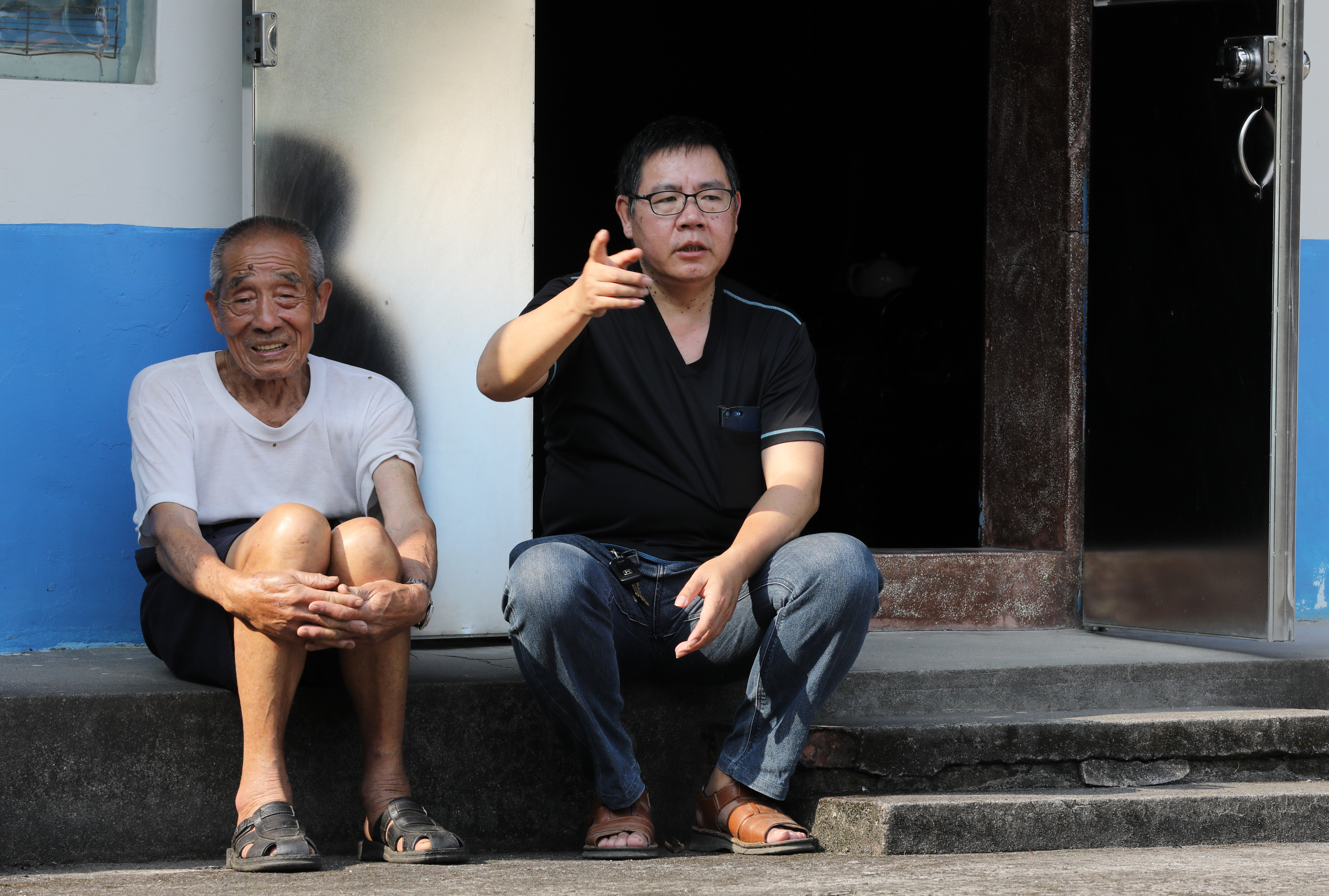 王榮發（右）和舅舅（左）一家就住在台七線馬路邊，20年來看盡村子變化，如今家門前每5分鐘就有一輛砂石車呼嘯而過。