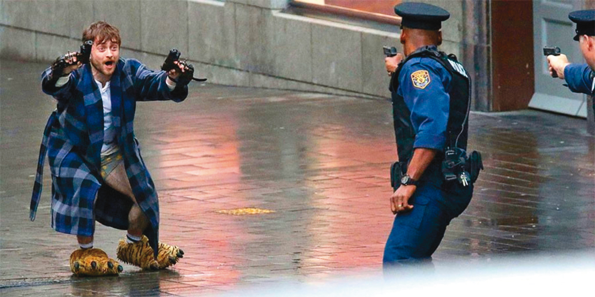 丹尼爾雷德克里夫披浴袍、踩拖鞋，雙手被釘上兩把上膛的手槍，在大街狂奔求生，整部片具備了邪典的惡趣潛力。（翻攝自imdb.com）