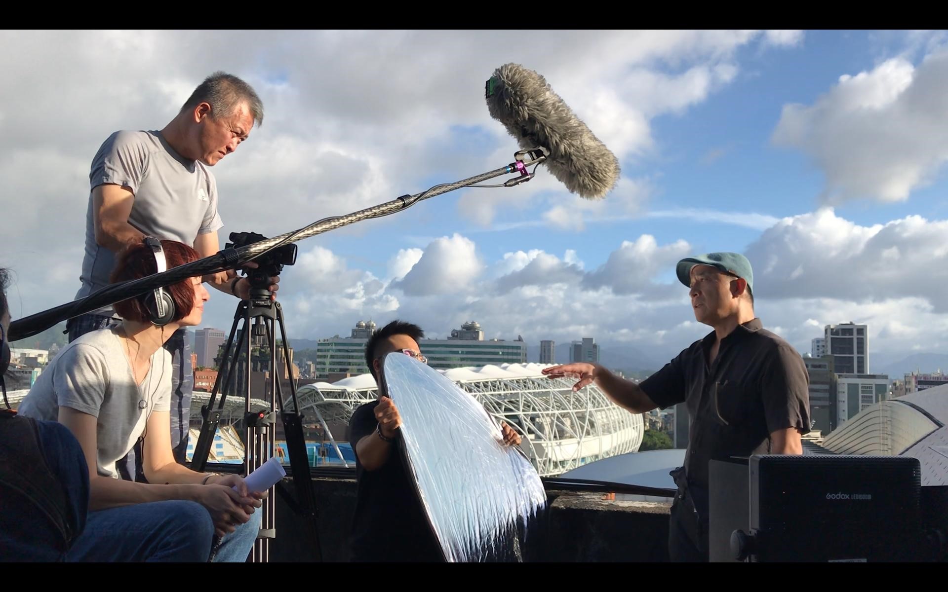 王婉柔（左前）訪問黃健和（右）時，攝影師韓允中（左後）想出在陽台拍攝的場景。（貝殼放大提供）