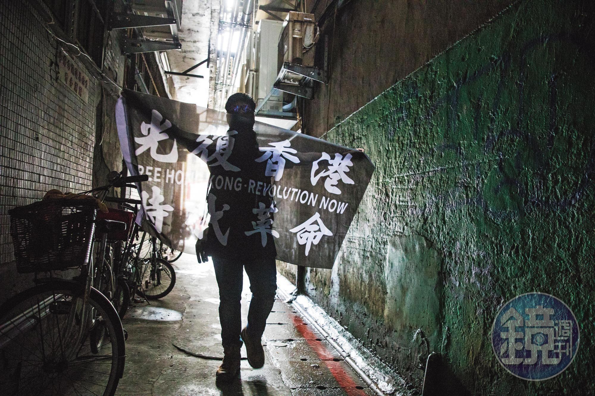 因反修例運動來台的港人中,不乏身分敏感者,他們自備面巾、頭套,全程蒙面受訪。圖為一名港人在台北的巷弄中,攤開自己設計、印製的「光復香港、時代革命」旗幟。