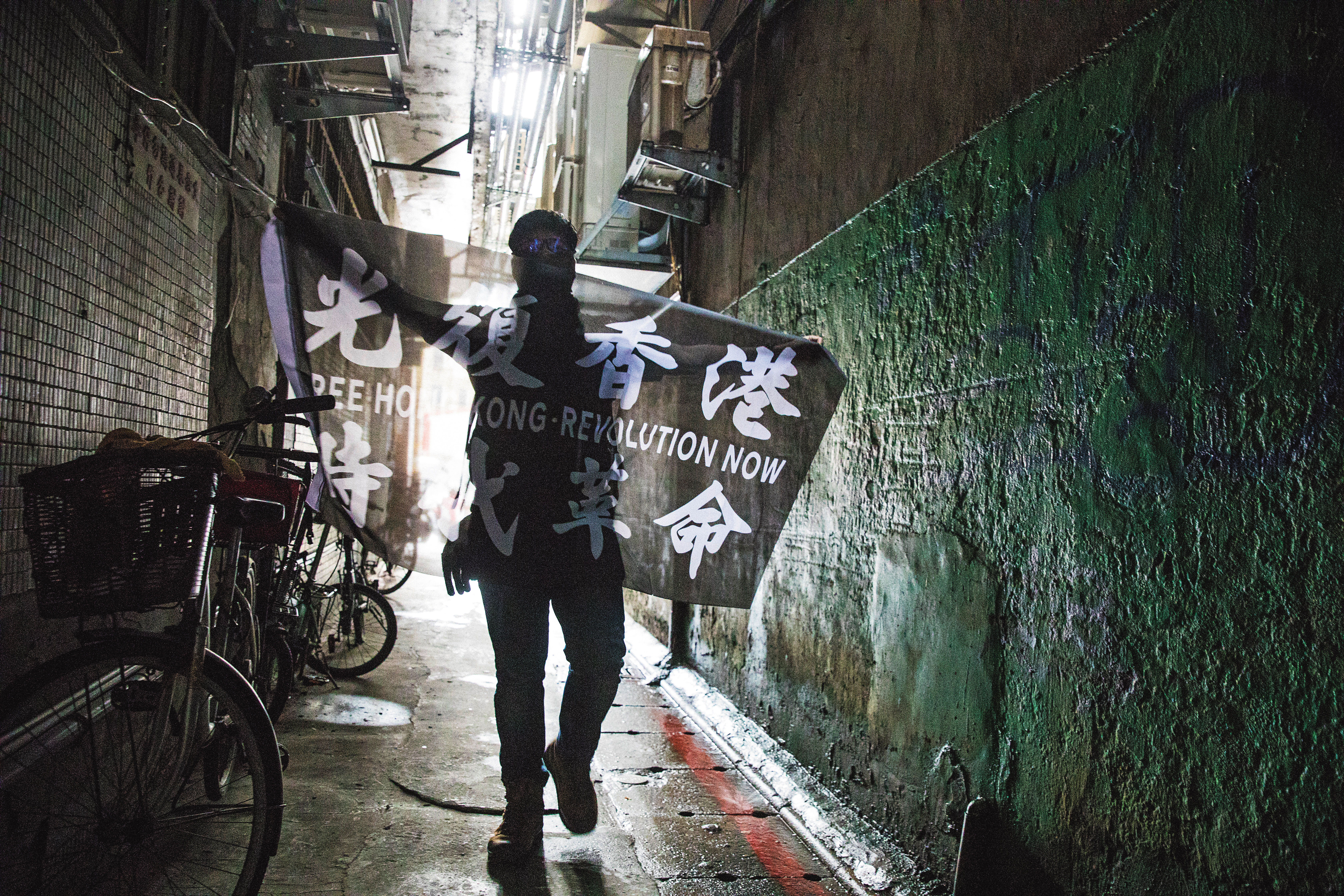 因反修例運動來台的港人中，不乏身分敏感者，他們自備面巾、頭套，全程蒙面受訪。圖為一名港人在台北的巷弄中，攤開自己設計、印製的「光復香港、時代革命」旗幟。