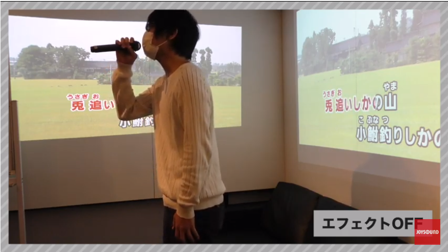 JOYSOUND官網上的影片，比較了戴口罩唱歌的情況下，加開音效口罩擴音效果與否產生的效果。影片中的男子便是本功能的開發者。（翻攝自JOYSOUND官網）