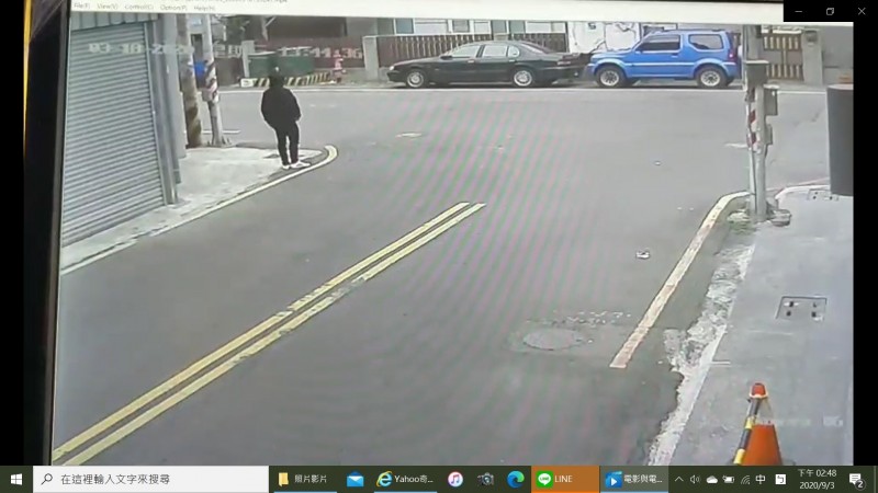 黃嫌旗下車手穿著一身黑衣在路口,等候拿取被害人丟棄在變電箱旁的手提袋。(翻攝畫面)