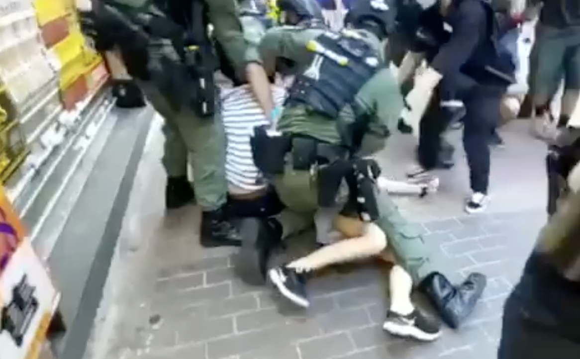 「906」九龍大遊行中,一名12歲女孩和家人上街購物,剛好經過遊行現場,竟被港警「騎身」壓倒在地。(翻攝科大電台新聞組影片)