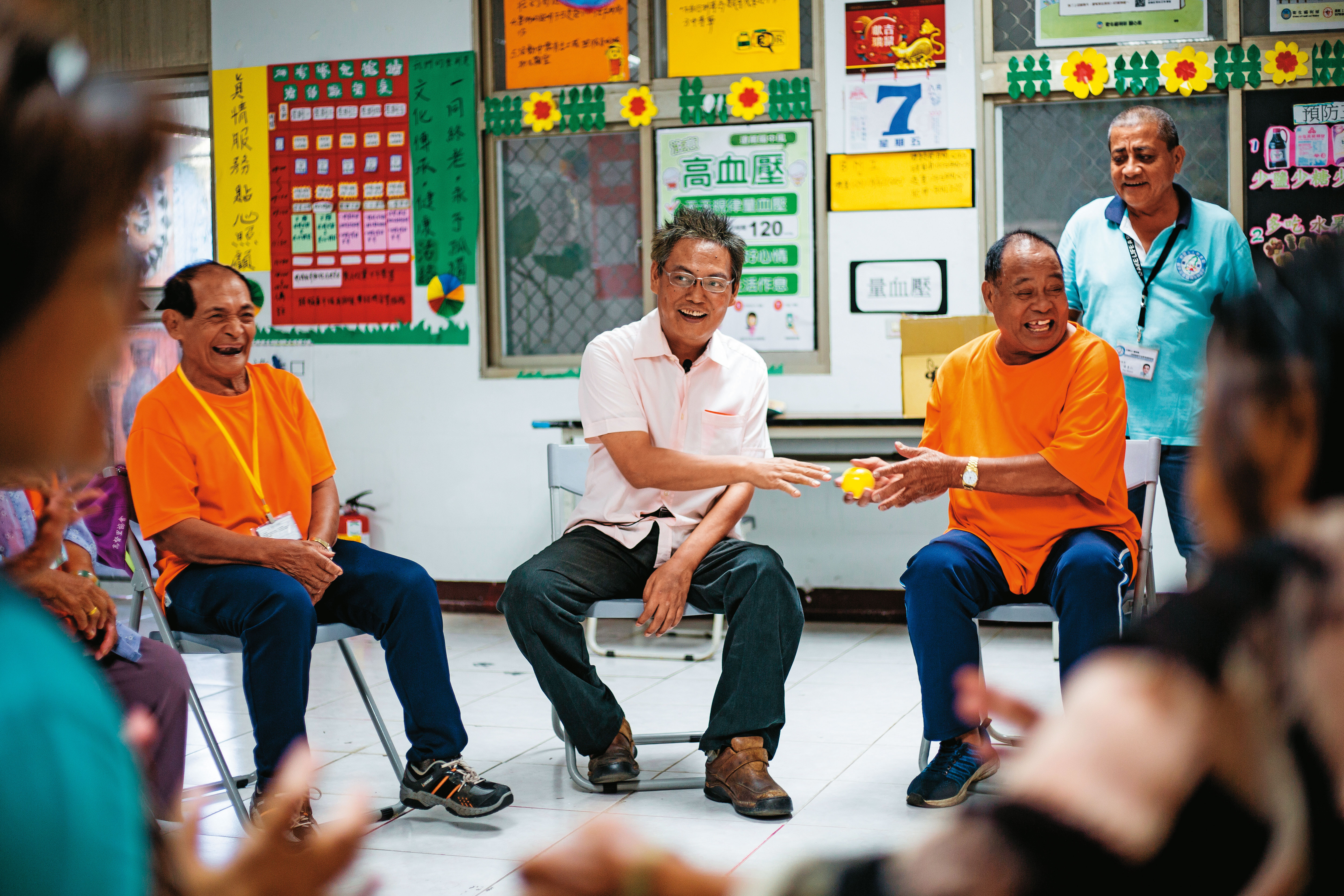 徐超斌（中）拜訪文健站，與老人們進行團康，身體不便的他仍努力融入傳球競賽。會後他送每人一包禮物，問他是什麼？他開玩笑說：「3年份保險套。」