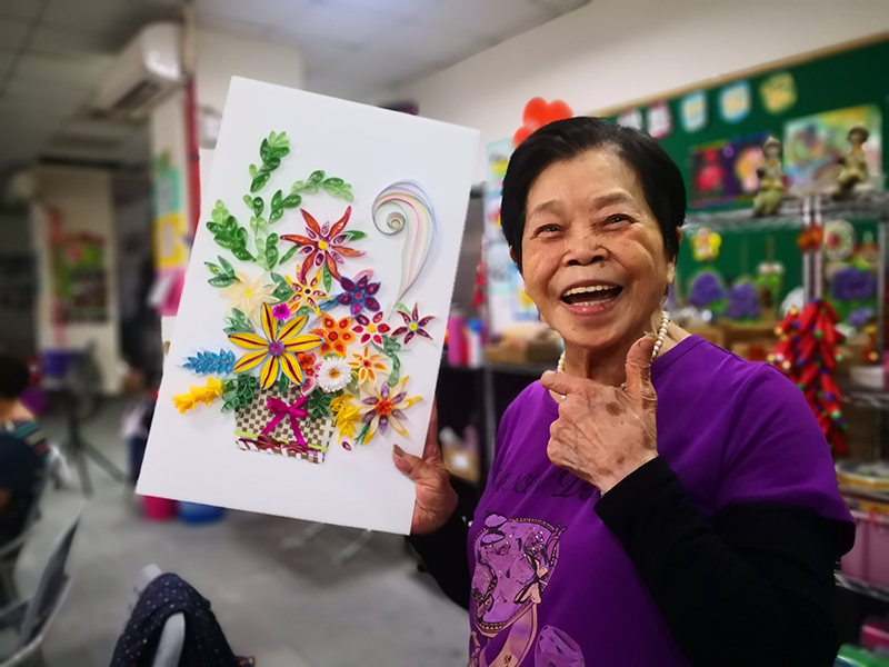 自由創作的捲紙畫配色縯粉，阿勉奶奶完成作品後笑開懷。（一粒麥子基金會提供）