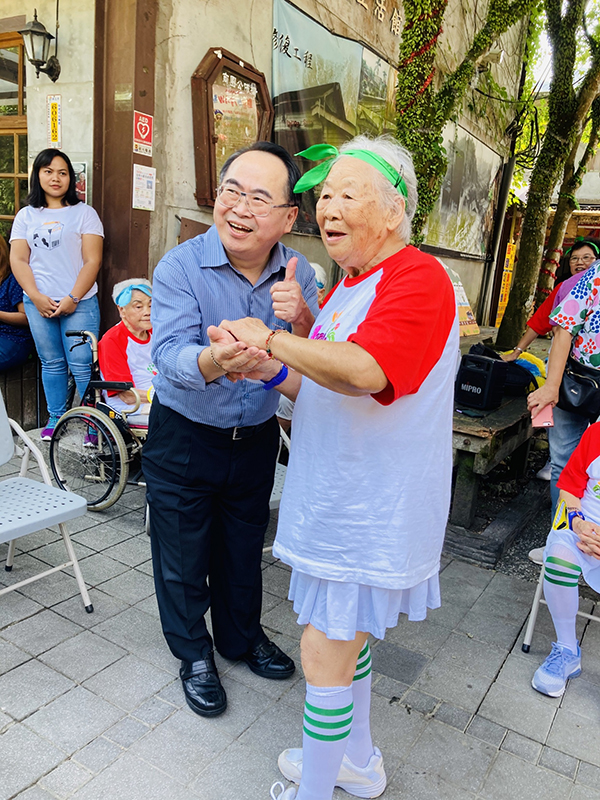 新北市社會局副局長林昭文（左）接受95歲奶奶親手編制手環祝福長壽健康。（一粒麥子基金會提供）