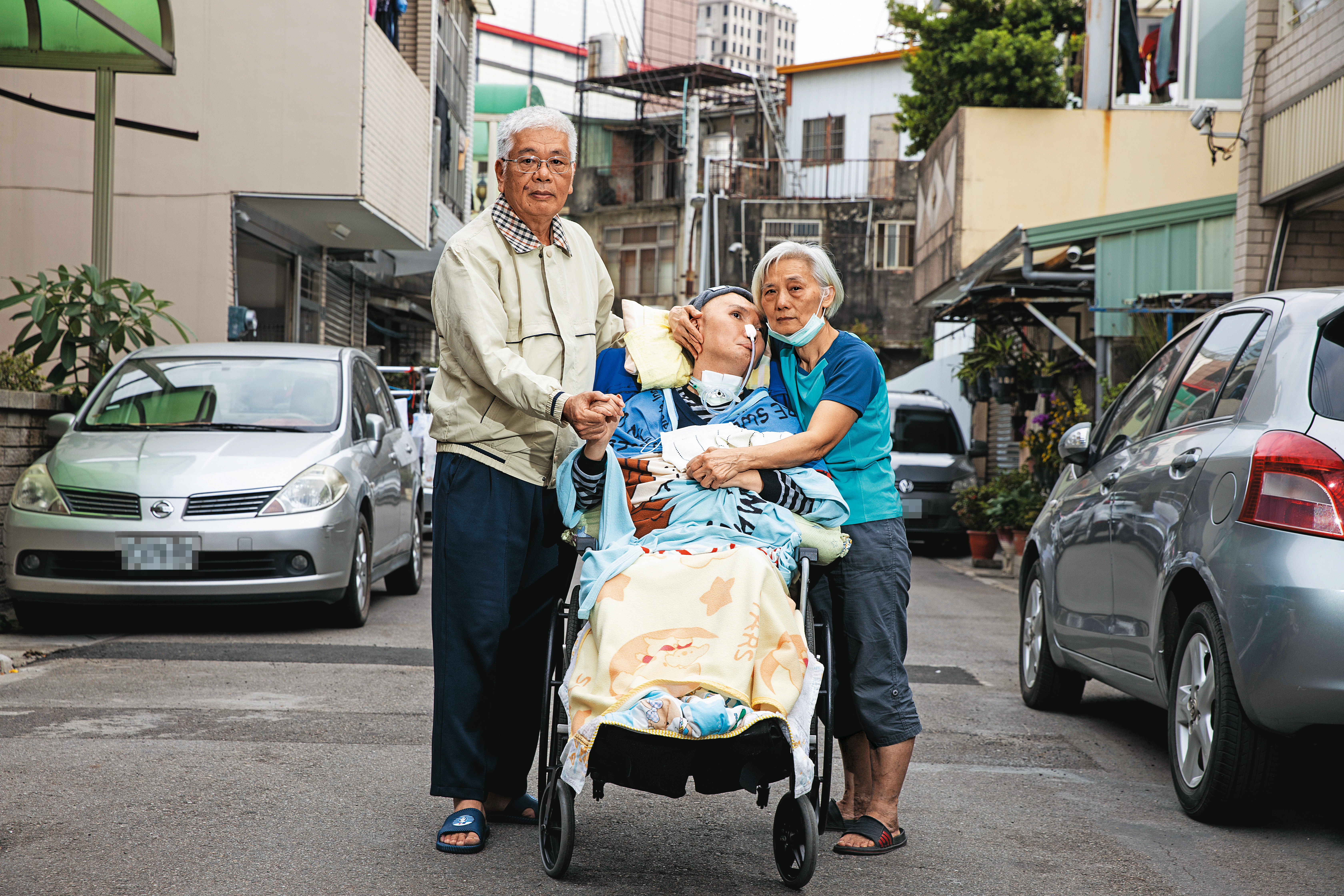 採訪這天，張爸（左）與張媽（右）帶張振聲（中）在家外巷子口散步。
