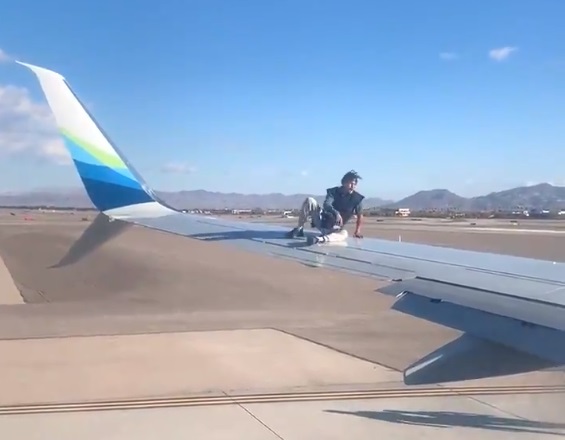一名行為脫序的男子跳上飛機機翼，他在機翼中段坐了下來，還對機內乘客擺弄姿勢。（翻攝自推特@mickakers）