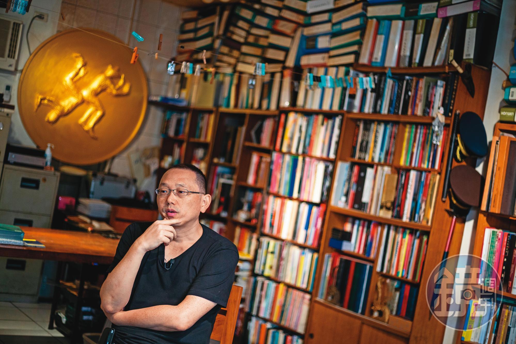 姚瑞中工作室(幻影堂)收藏了許多藝術書籍與展冊文獻,他身後的金色圓徽是他為今年大型個展《犬儒共和國》設計的國徽。