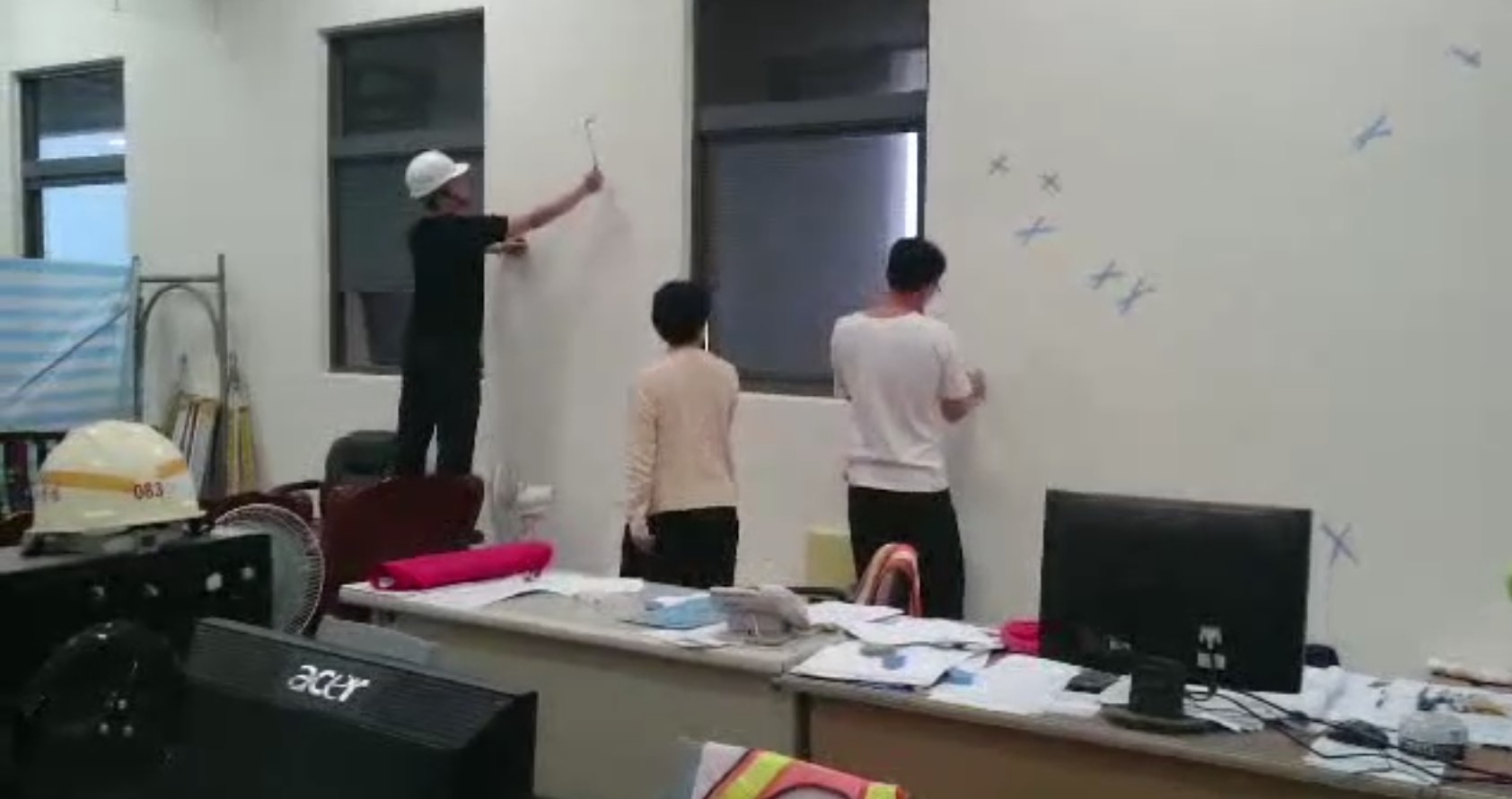 替代役男拿著鎚子敲牆壁,協助主驗官找出異音的位置。(讀者提供)