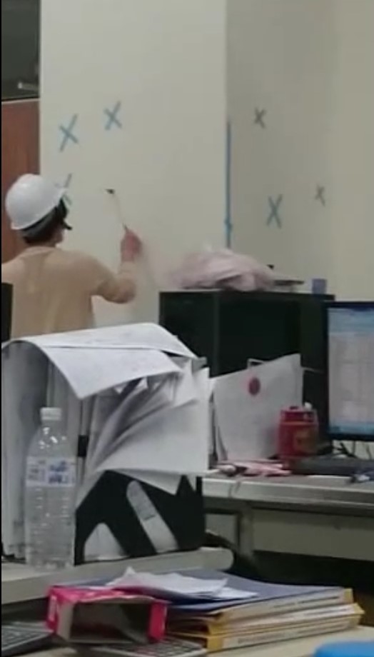驗收時，主驗官群拿著鎚子四處敲打牆面。（讀者提供）