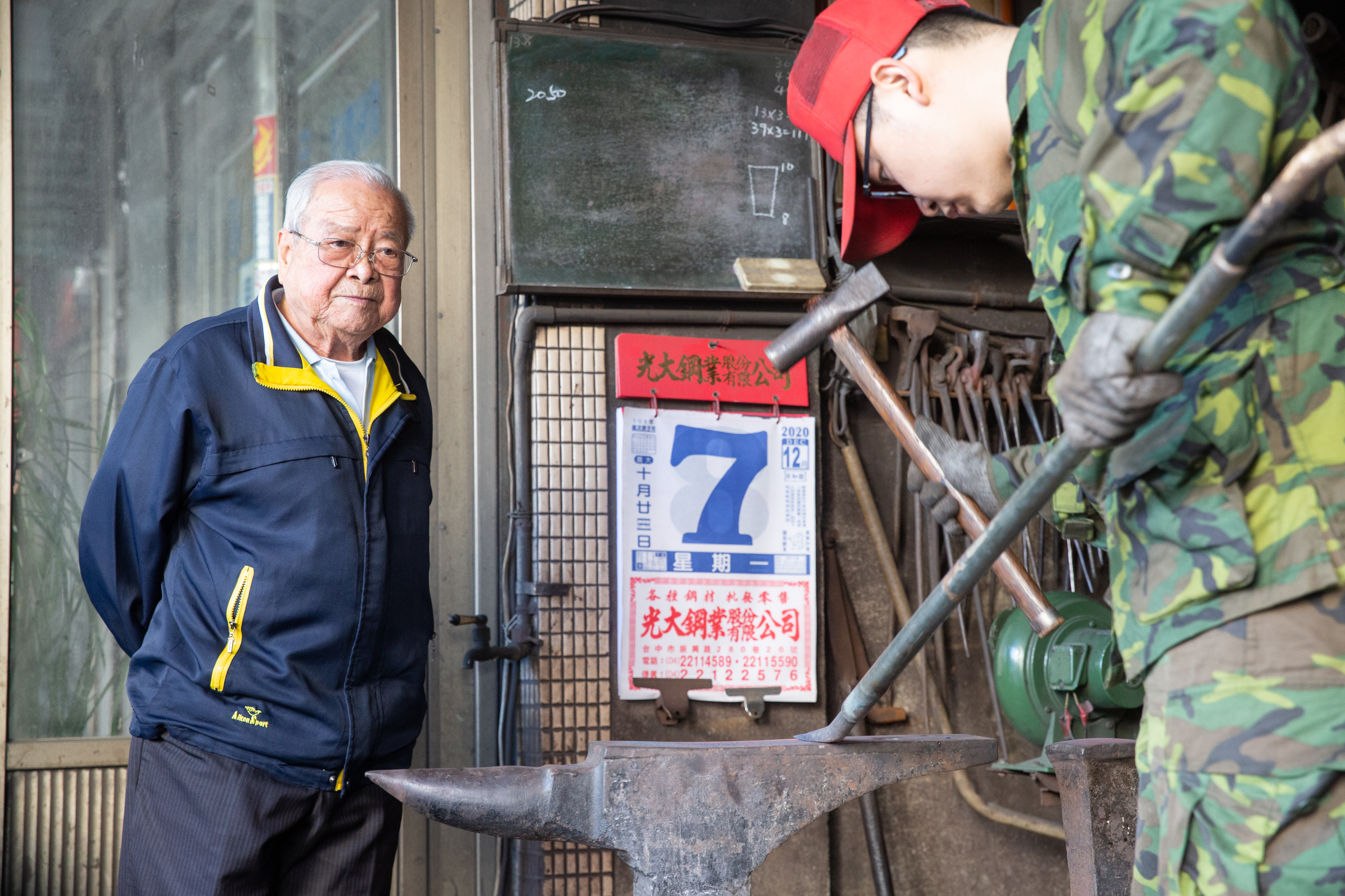 蔡進永的阿公、第一代蔡慶隆（左）雖已退休，仍常到店面看孫子（右）打鐵。