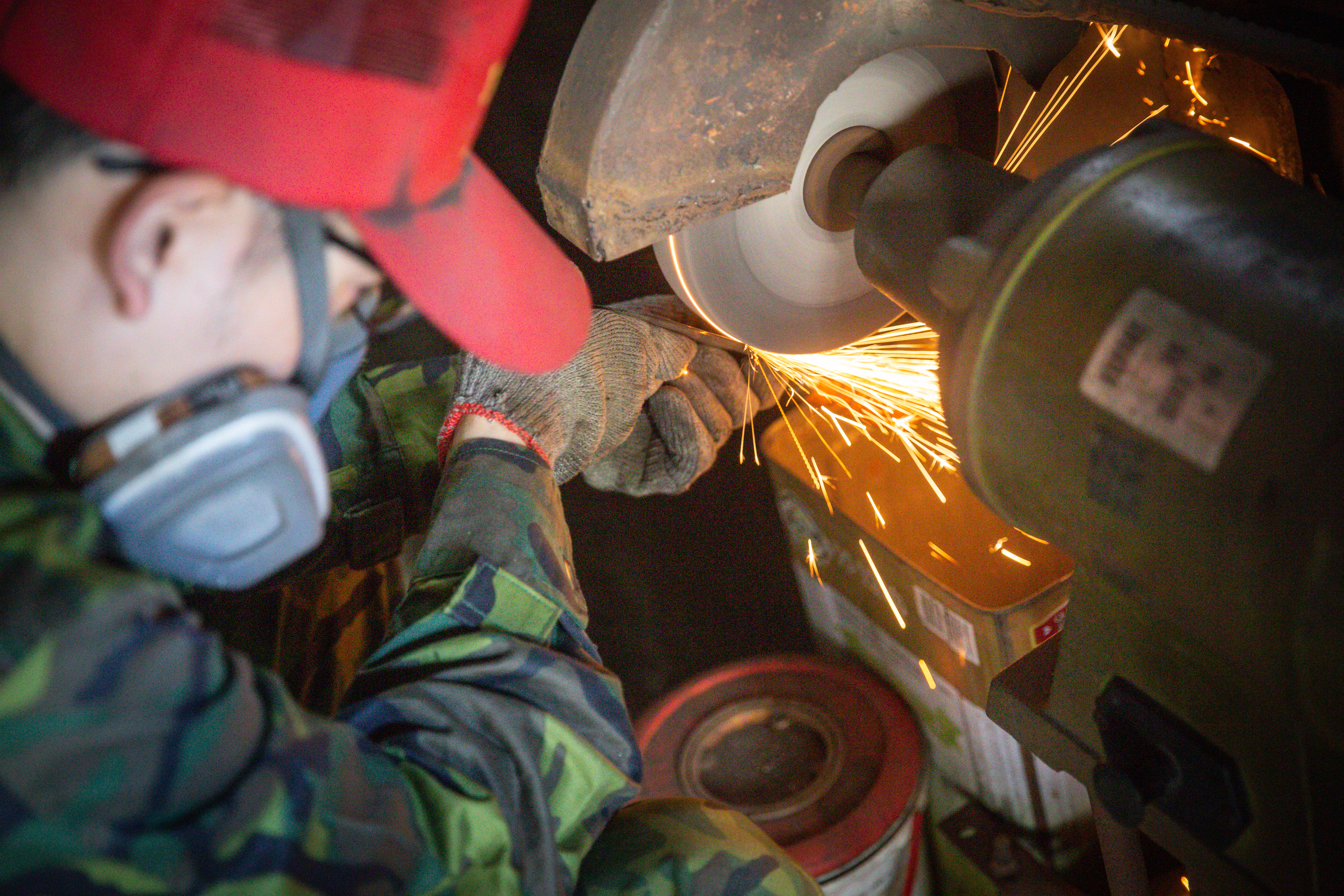 第三代蔡進永身著耐髒的迷彩服打鐵，頭戴防毒面罩，以防吸進粉塵。