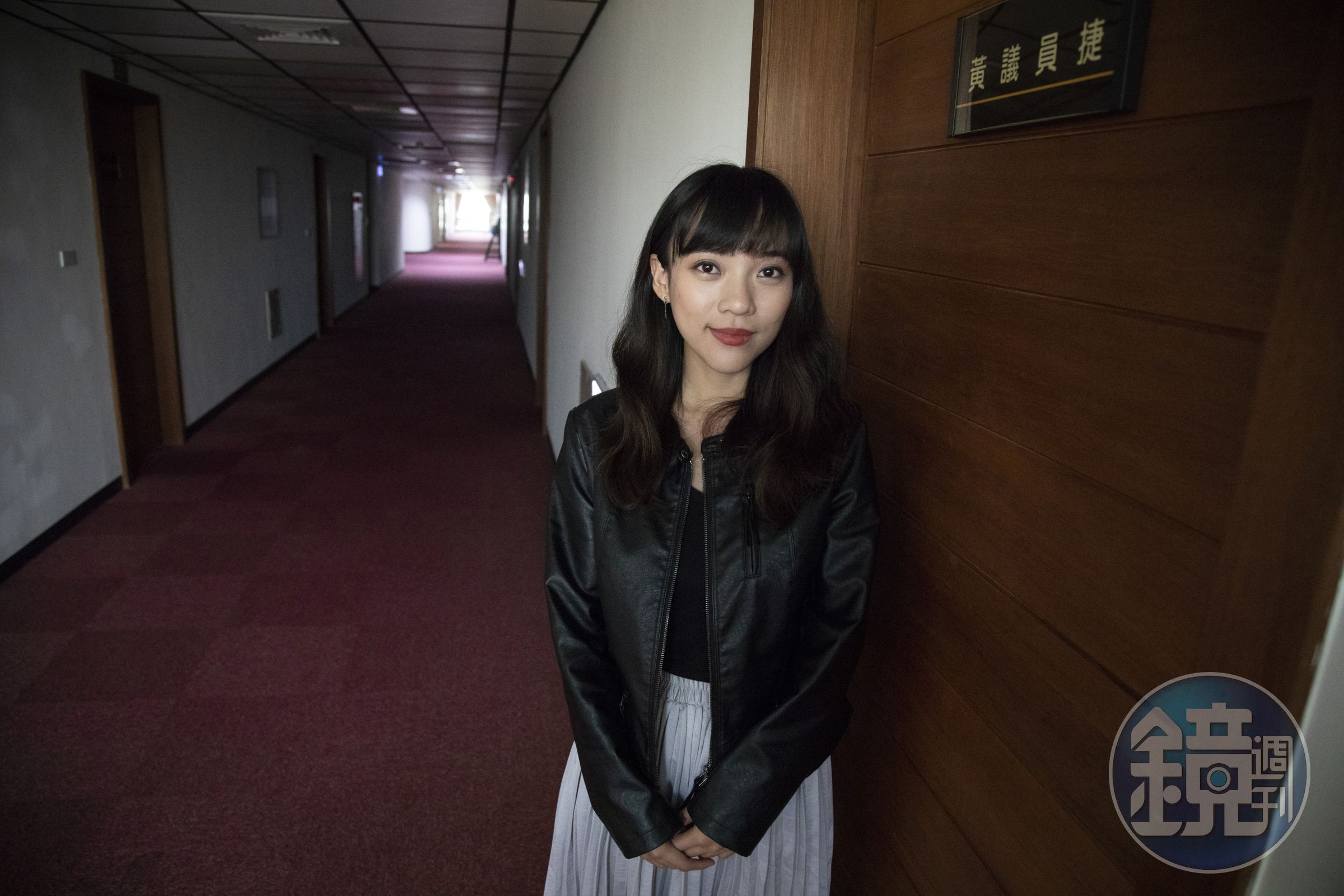 黃捷站在議會辦公室門口，辦公室內有許多社運議題、同婚的標語，除此之外相當簡樸。