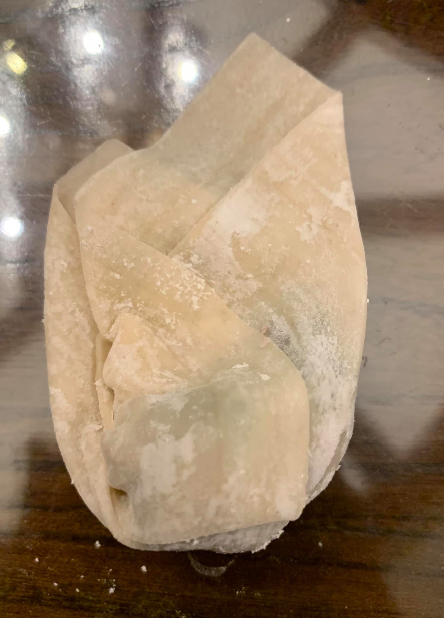 包薺菜餛飩步驟四：兩頭向中扭折成包袱狀，兩巾對齊沾水緊捏即可收口。