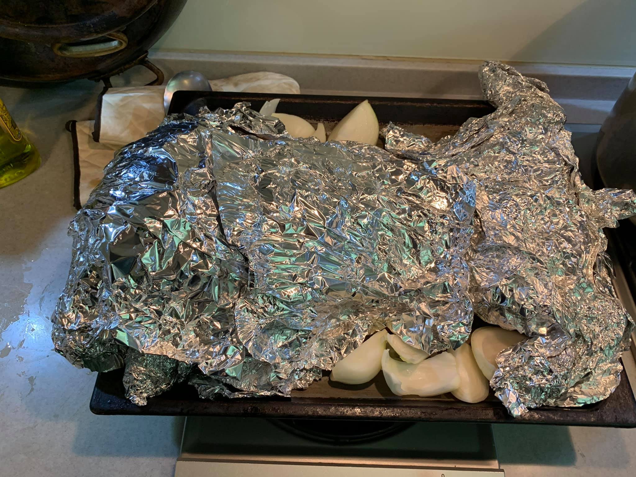 烤盤鋪上洋蔥，放上乳豬，包裹住鋁箔紙。