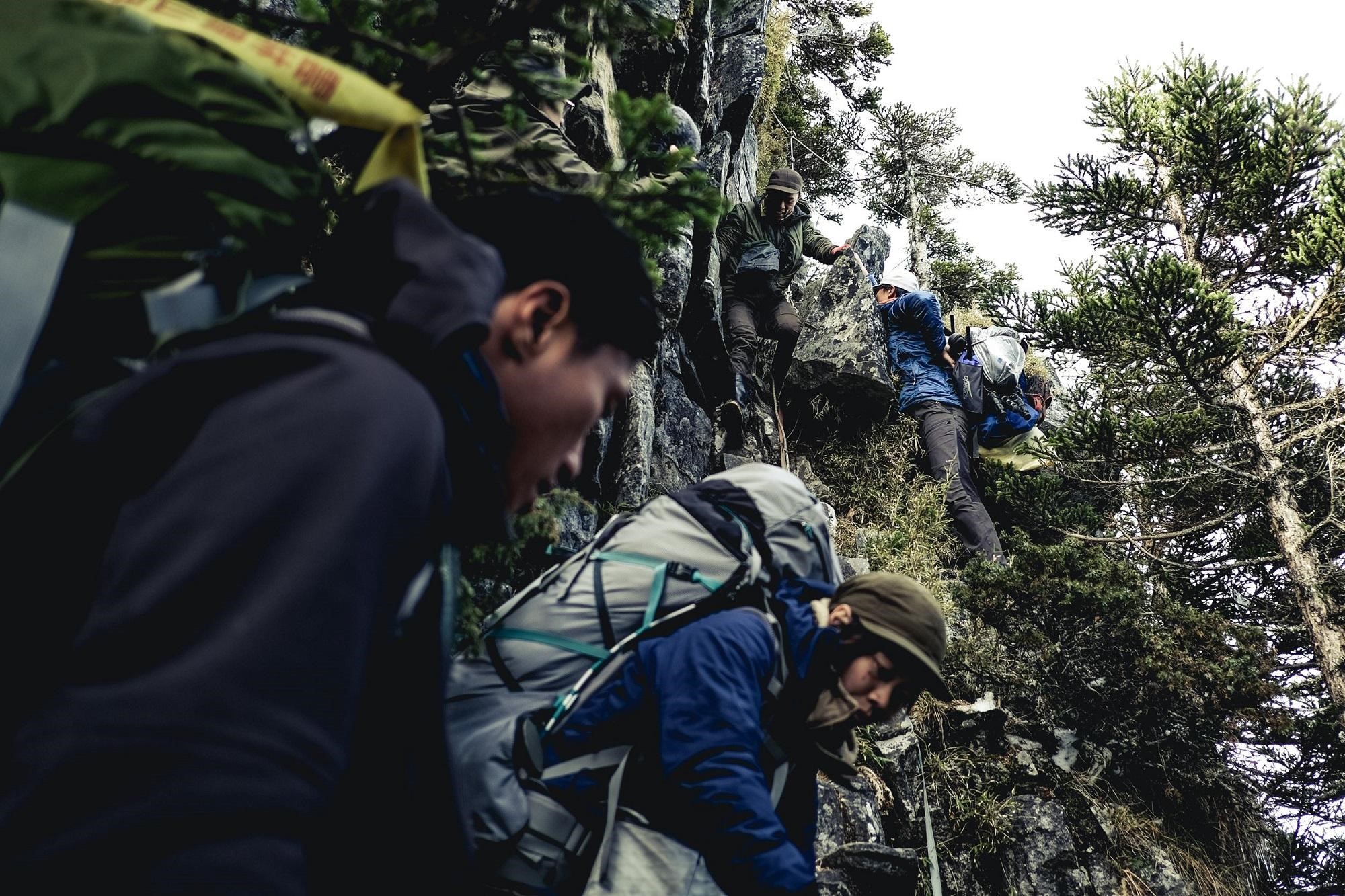 工作人員負重在懸崖邊的岩石攀爬，經常得手腳並用。（公視提供）
