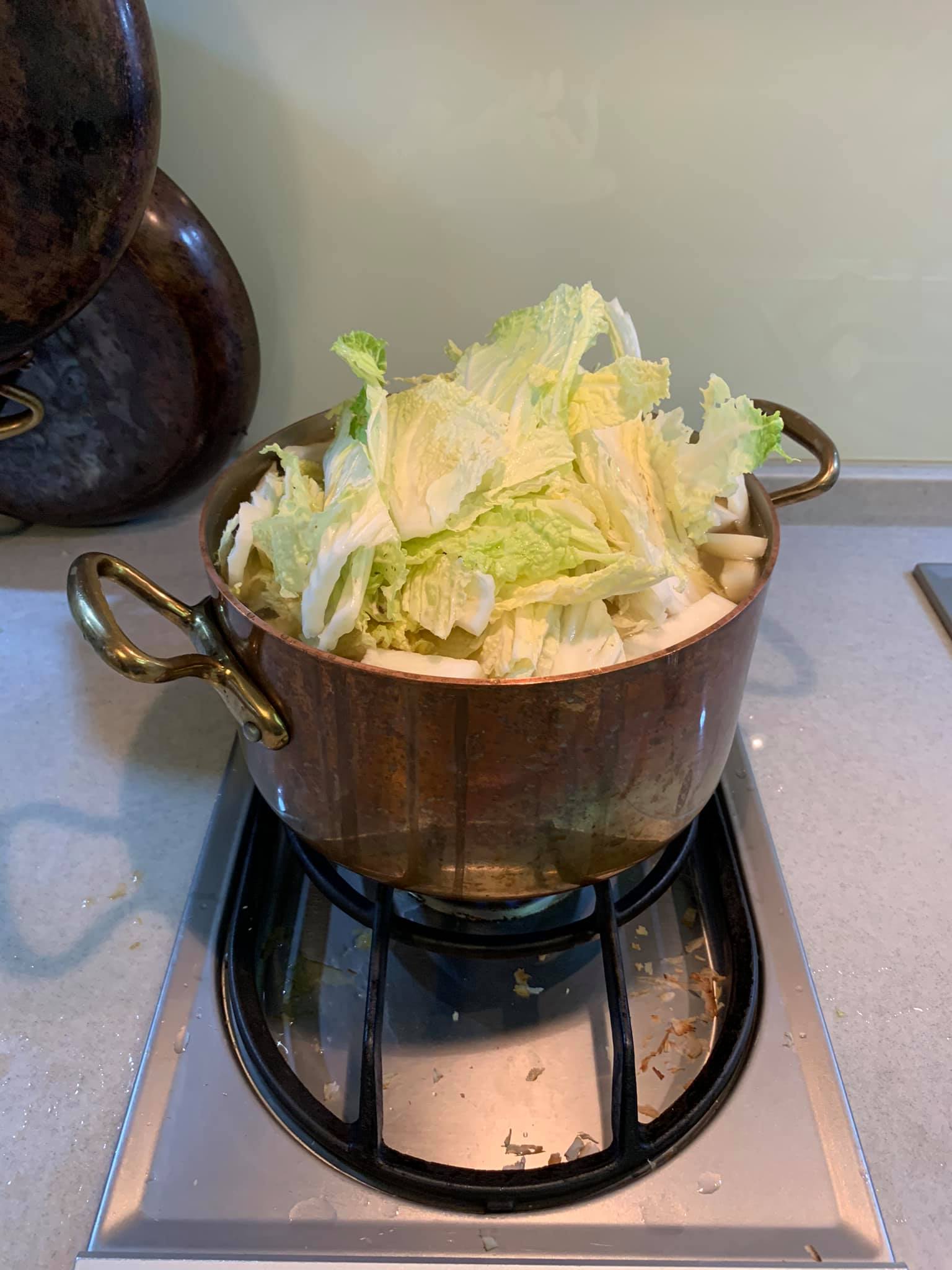 把炒軟的蔬菜放入大銅鍋中，加入大白菜與泡香菇的水。