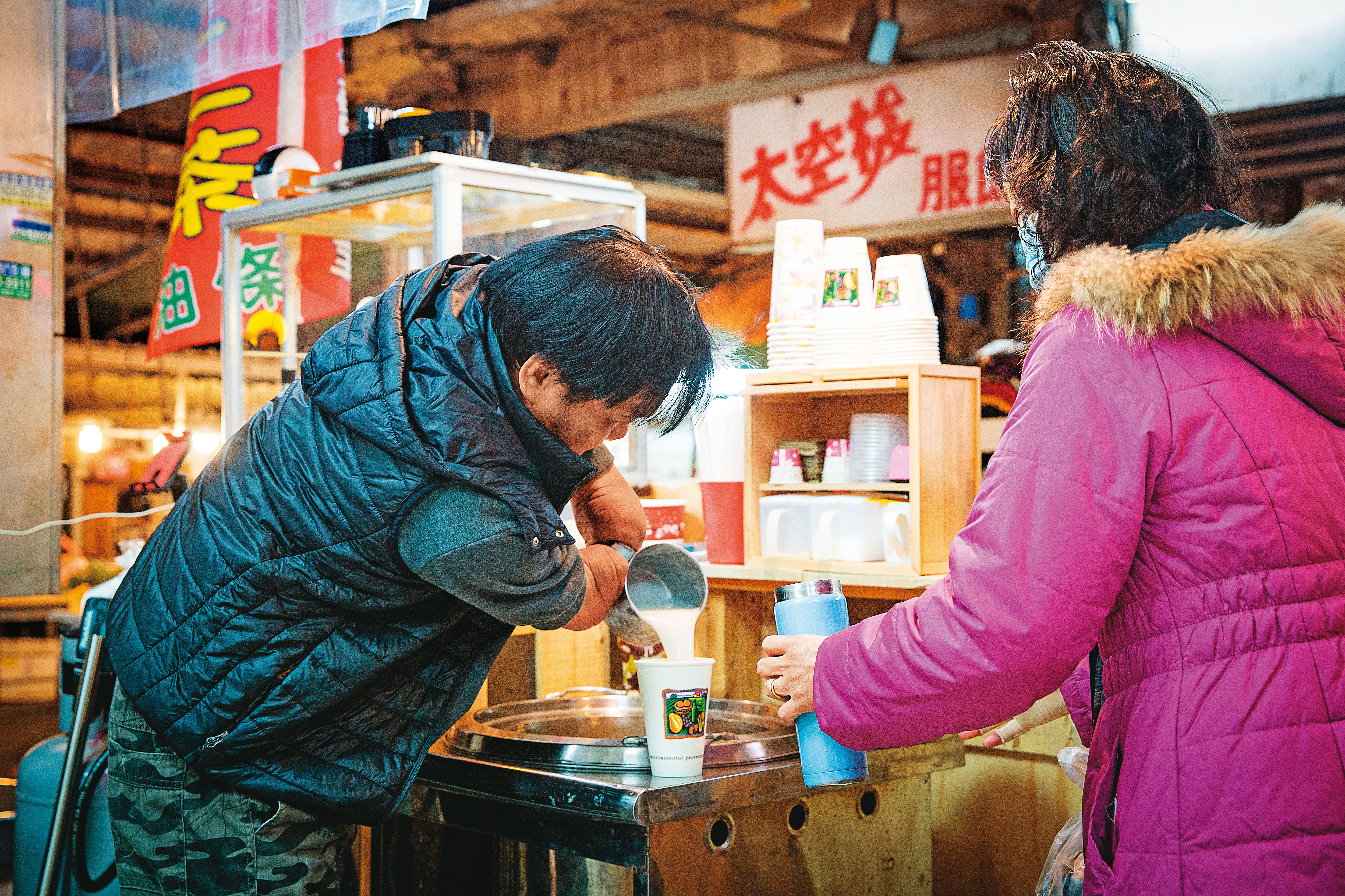 林建民（左）雖然截肢，但用鋼杯舀杏仁湯、裝杯都難不倒他。