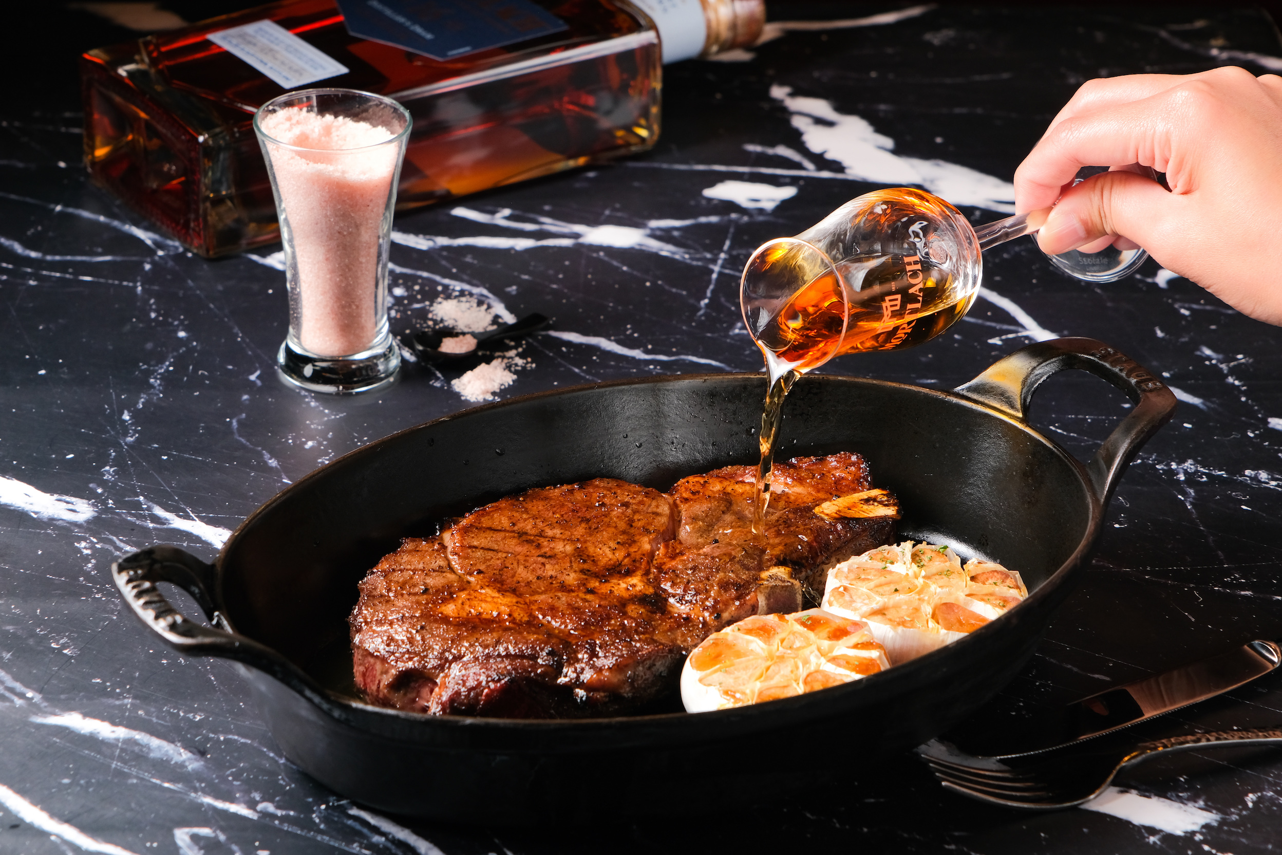 「炙烤美國頂級帶骨肋眼牛排」將慕赫2.81-16年單一麥芽威士忌淋入鑄鐵鍋中，以酒香火焰炙烤表面。（慕赫限定套餐，單點2,400～2,800元/份，每日限量）