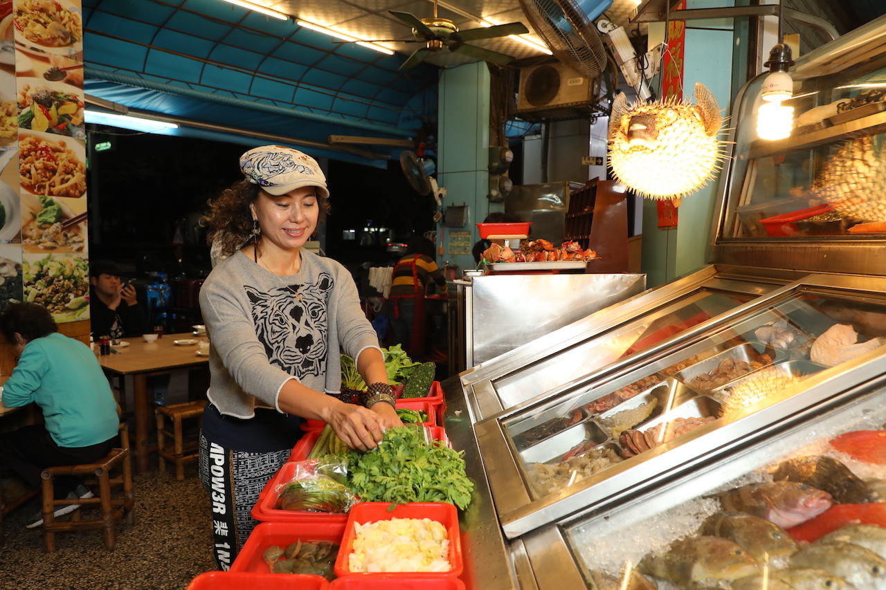 「海味澎湖活海產」每天傍晚起點亮招牌燈，老闆王雪燕在檯子擺滿澎湖魚貝和蔬菜。