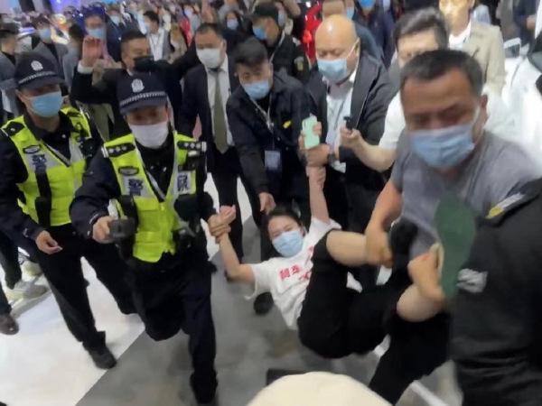 張女不顧工作人員勸阻爬上車頂,重複大喊「特斯拉煞車失靈」,最後被保全拖離現場。(翻攝微博)