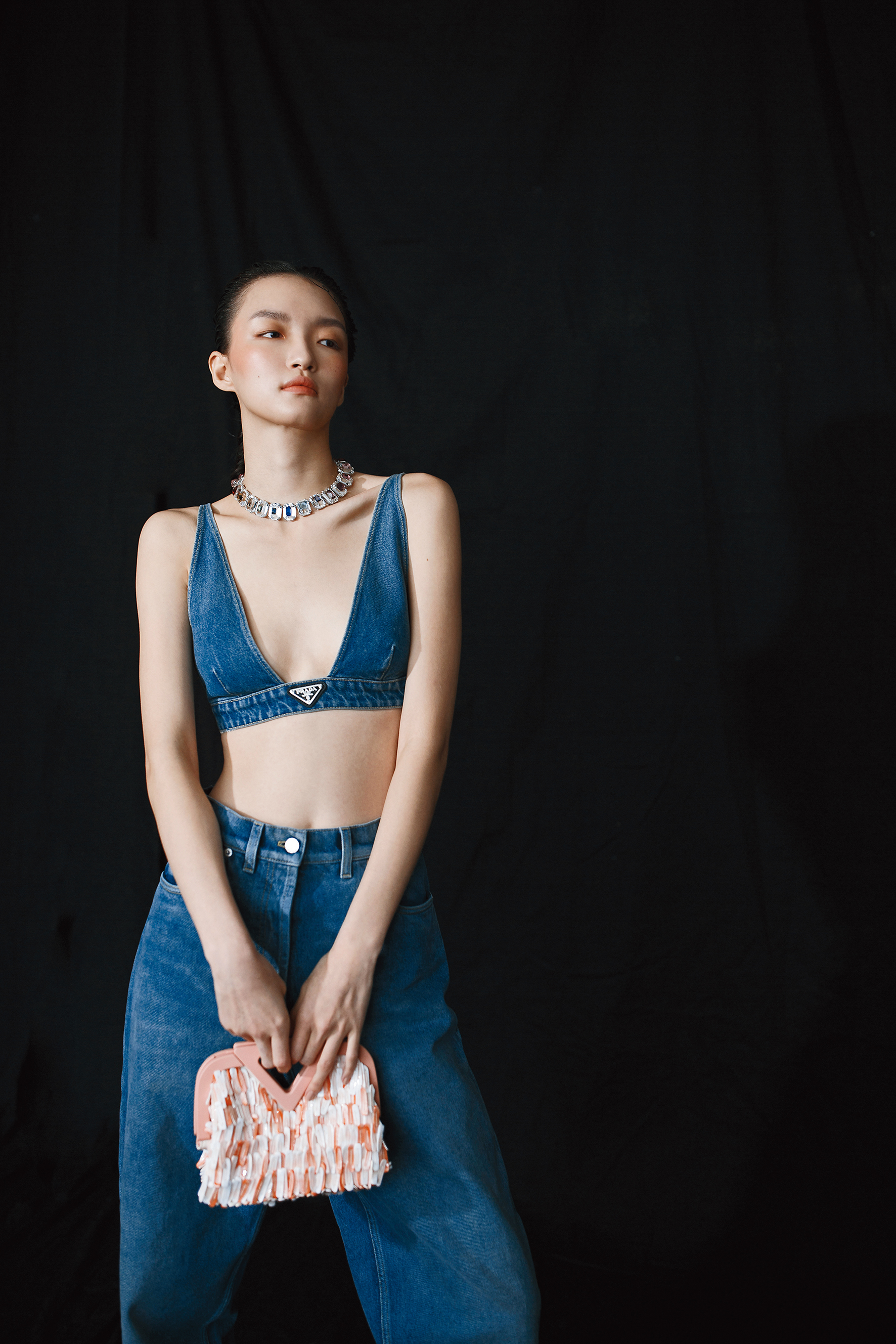 馬卡龍粉鳳凰螺貝殼手提袋 NT$196,200 by BOTTEGA VENETA；有機丹寧背心 NT$17,000 by PRADA；有機直筒牛仔褲 NT$31,500 by PRADA；Chroma頸鍊 NT$31,900 by SWAROVSKI。