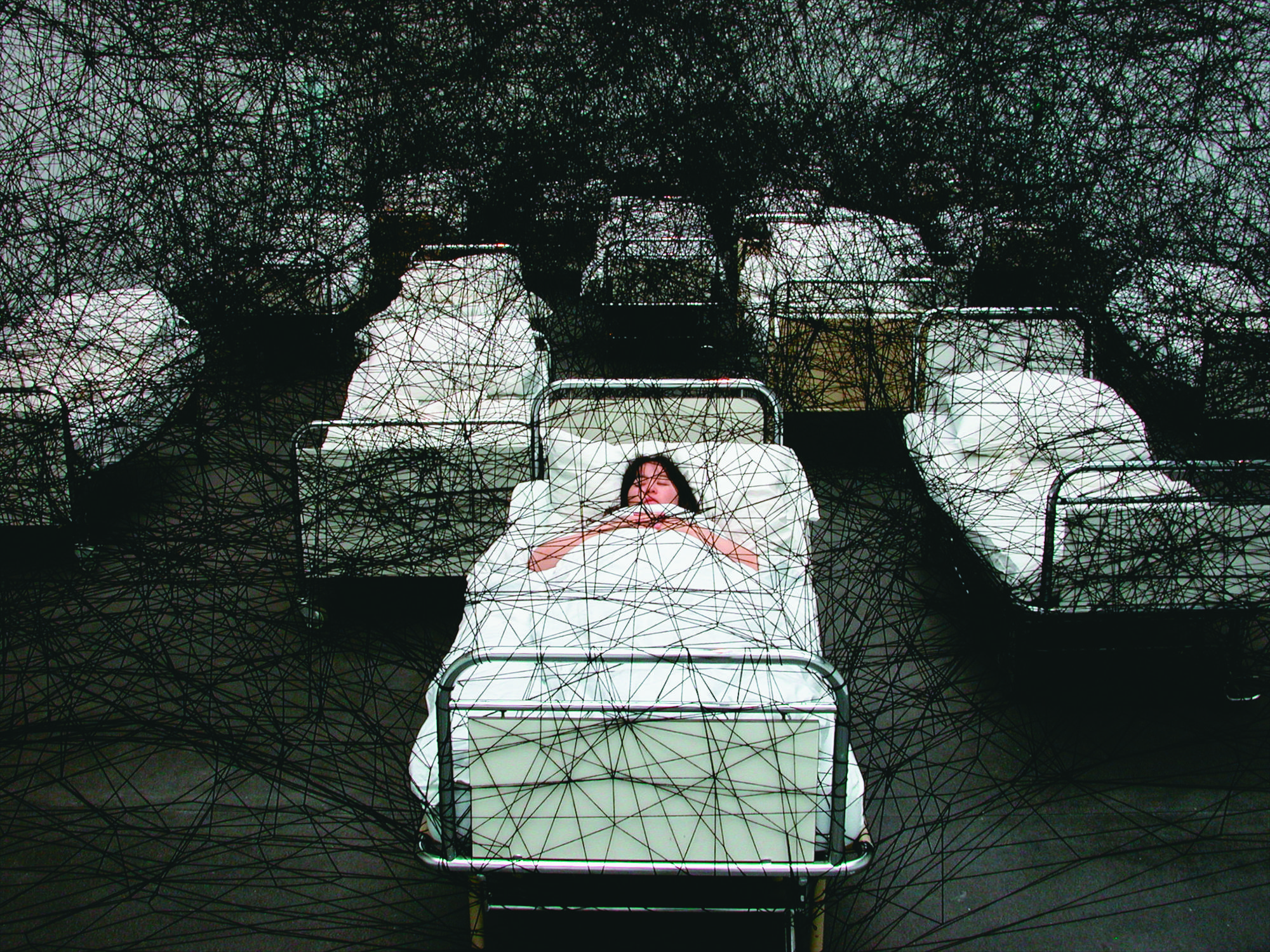 塩田千春結合裝置與行為的作品〈在沉睡中〉(During Sleep),她躺在床上睡覺,床則象徵了人生的起點與終點。(塩田千春提供)