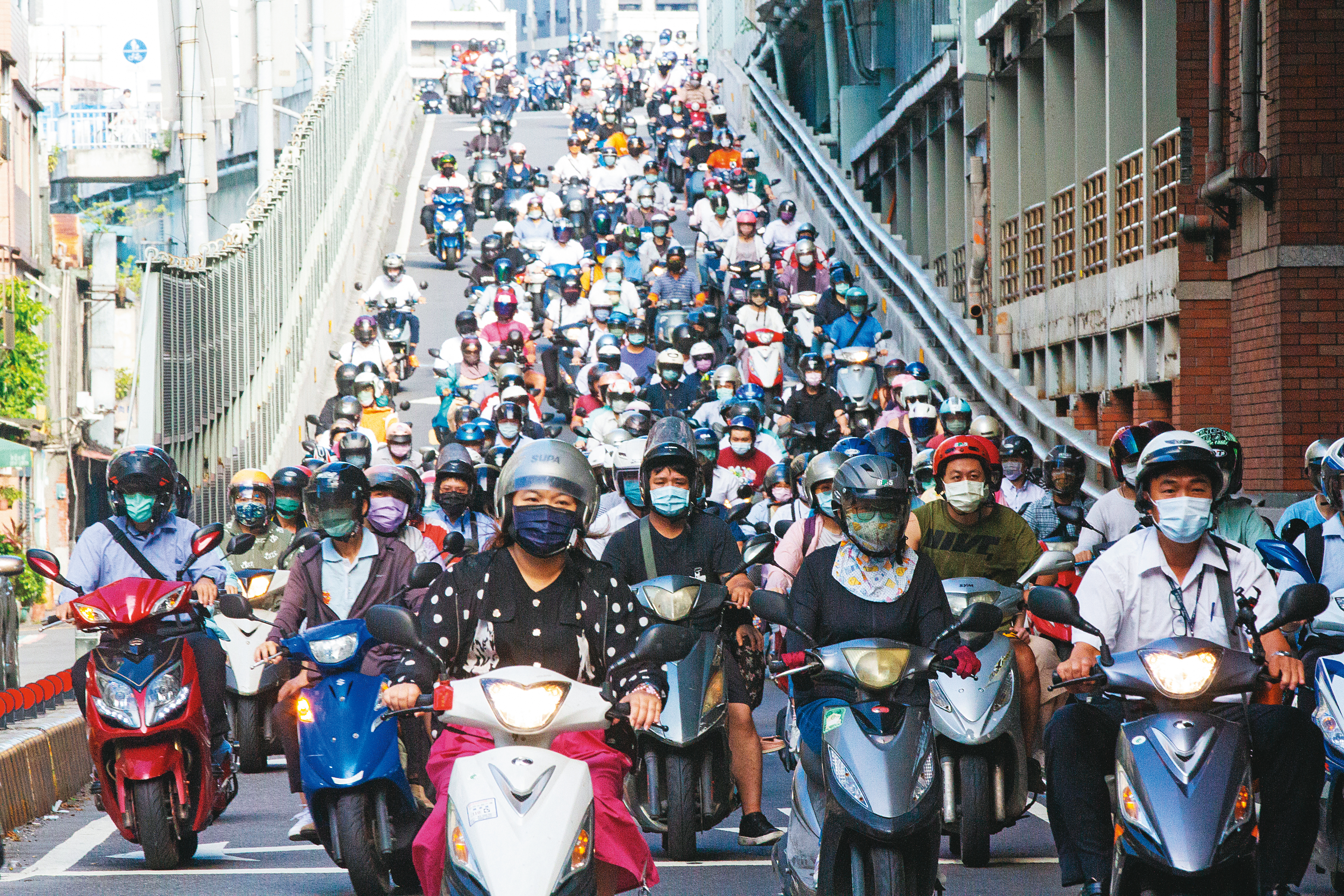 疫情期間，往返雙北的機車騎士緊緊戴上口罩。隨著警戒有望降級，政府研議相關配套措施，而口罩仍被視為是防疫最後防線。