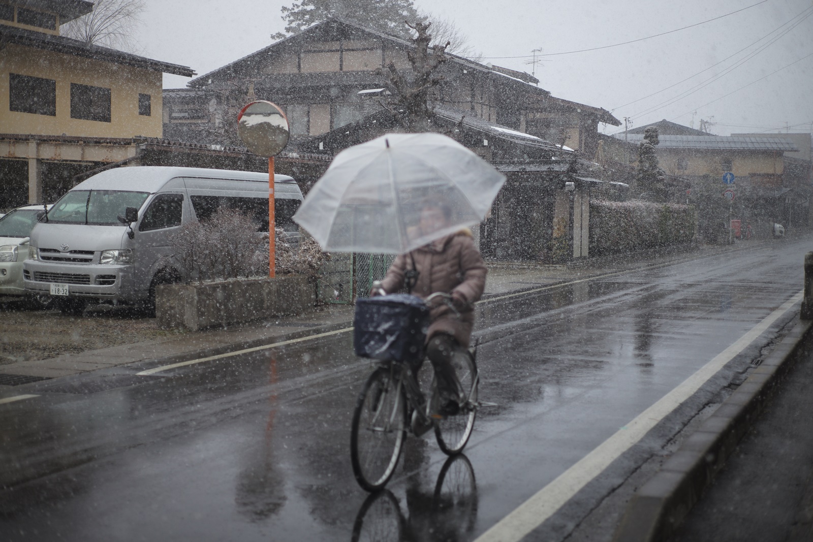 婦人打著傘騎車經過下大雪的街道。