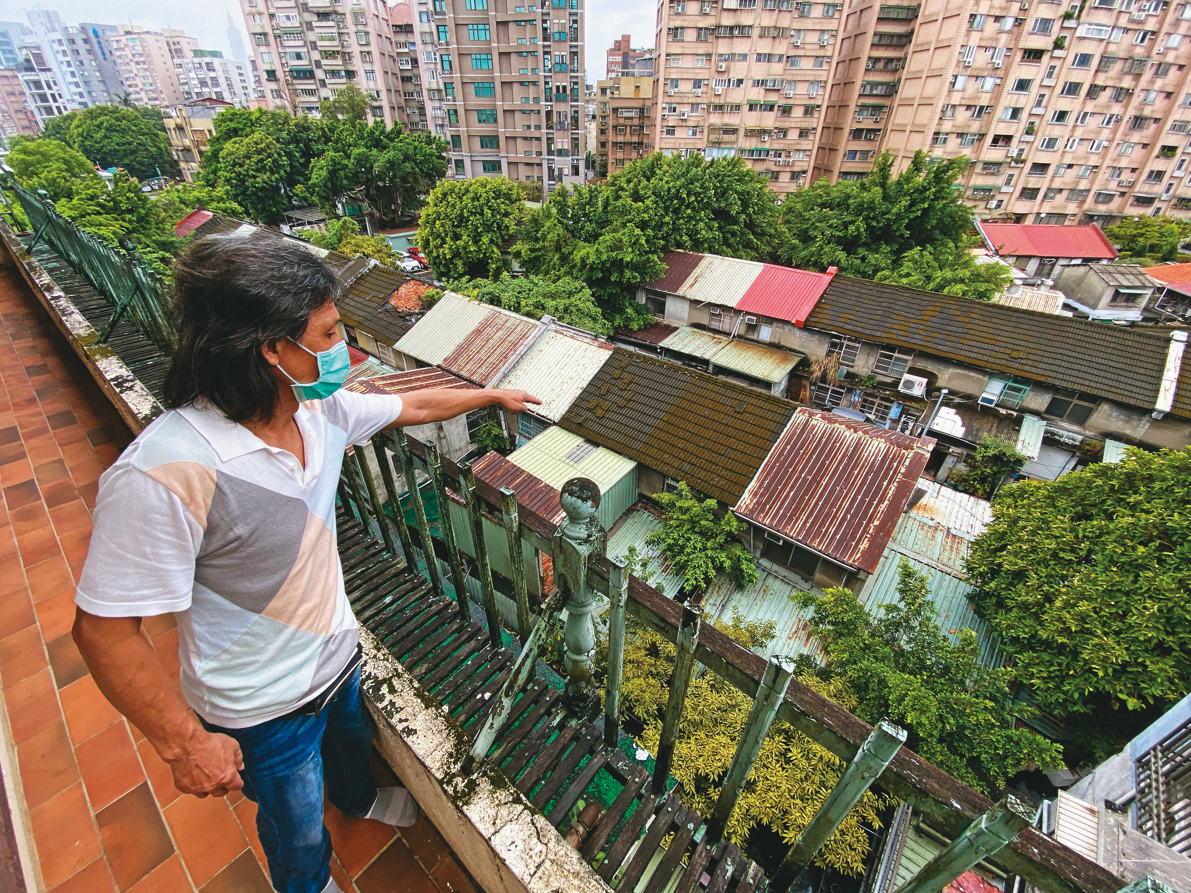 王姓住戶站在屋齡49年的老公寓，指著眼前即將都更的忠誠新村，希望北市府能將他們納入都更範圍。