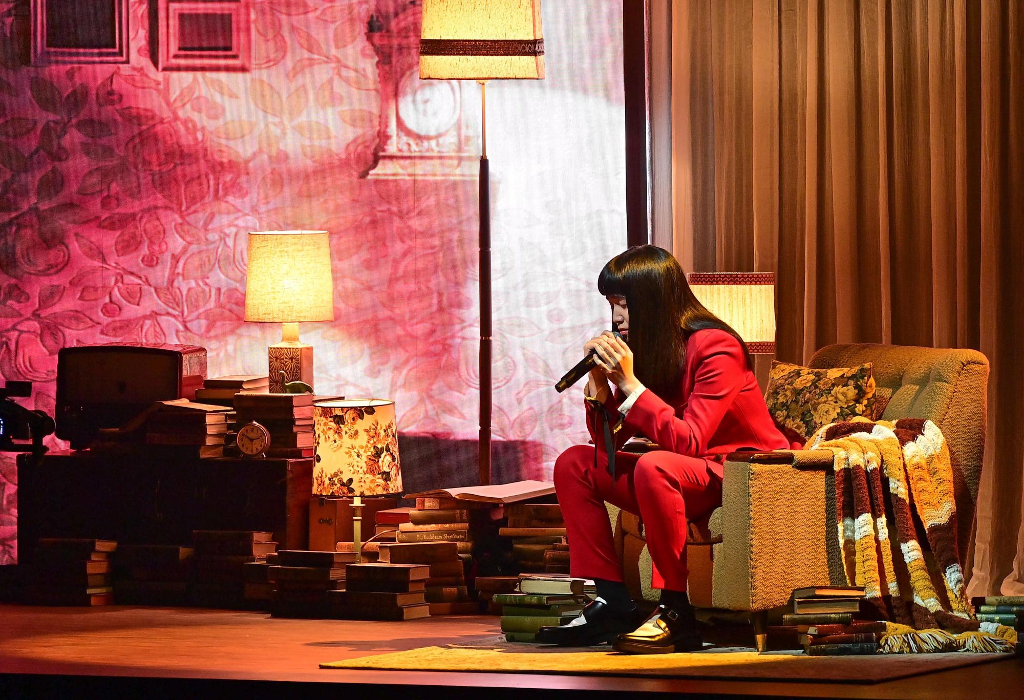 持修穿著一身酒紅色西裝登台表演,坐在背景沙發上演唱〈血肉〉。(台視提供)
