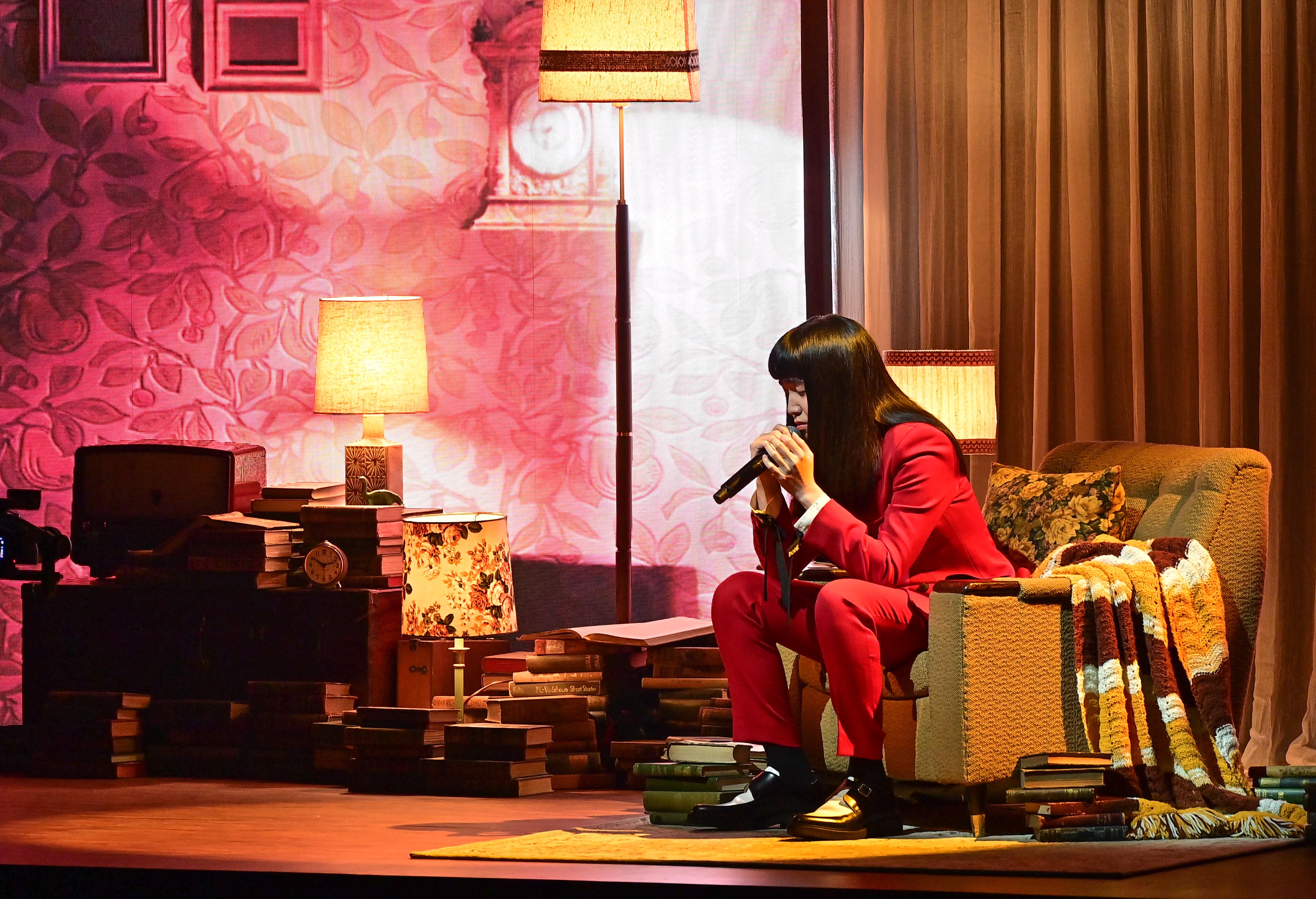 持修穿著一身酒紅色西裝登台表演,坐在背景沙發上演唱〈血肉〉。(台視提供)