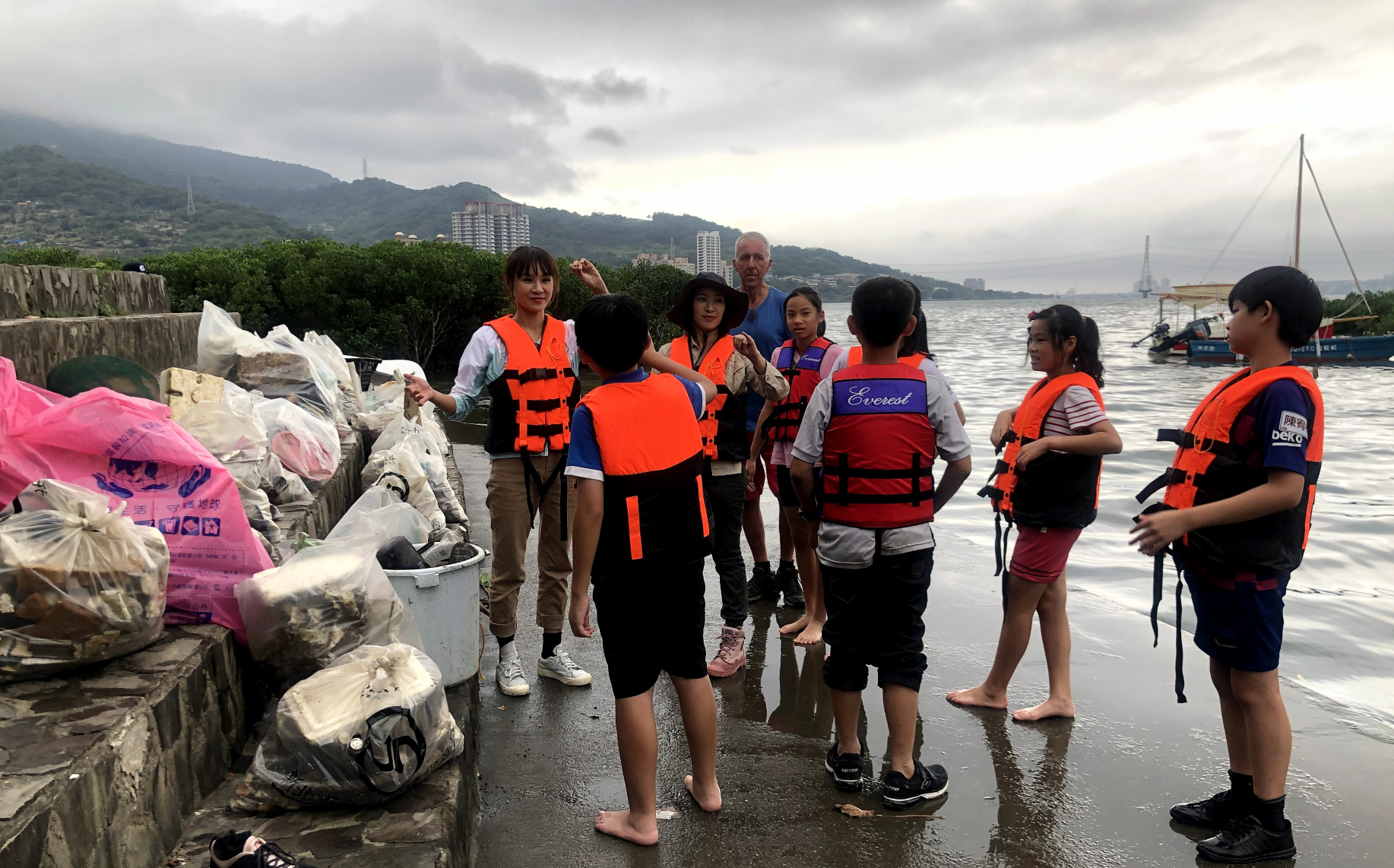 亞里(後排左1)、湘涵(後排左2)和小小背包客找到在淡水河划獨木舟撿垃圾的英國人Peter Lowe(後排左3)一起清理紅樹林,並後續做垃圾分類。(公視提供)