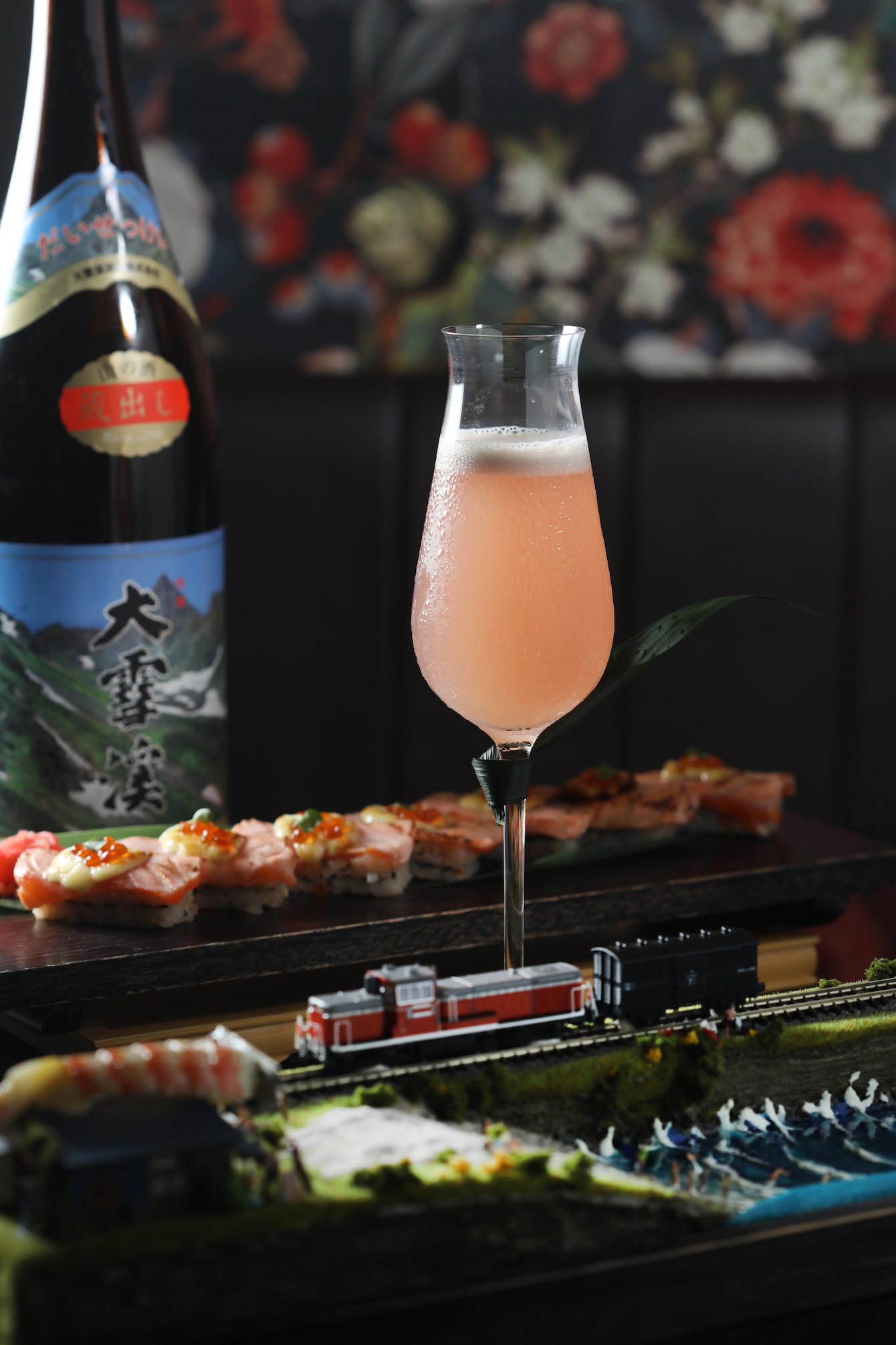 「一斤染」（前，280元／杯）以清酒、荔枝奶酒加入玫瑰糖漿與薑糖，搭配「焦糖鮭魚火車箱壽司」（後，單點箱壽司360元／份）特別合味。