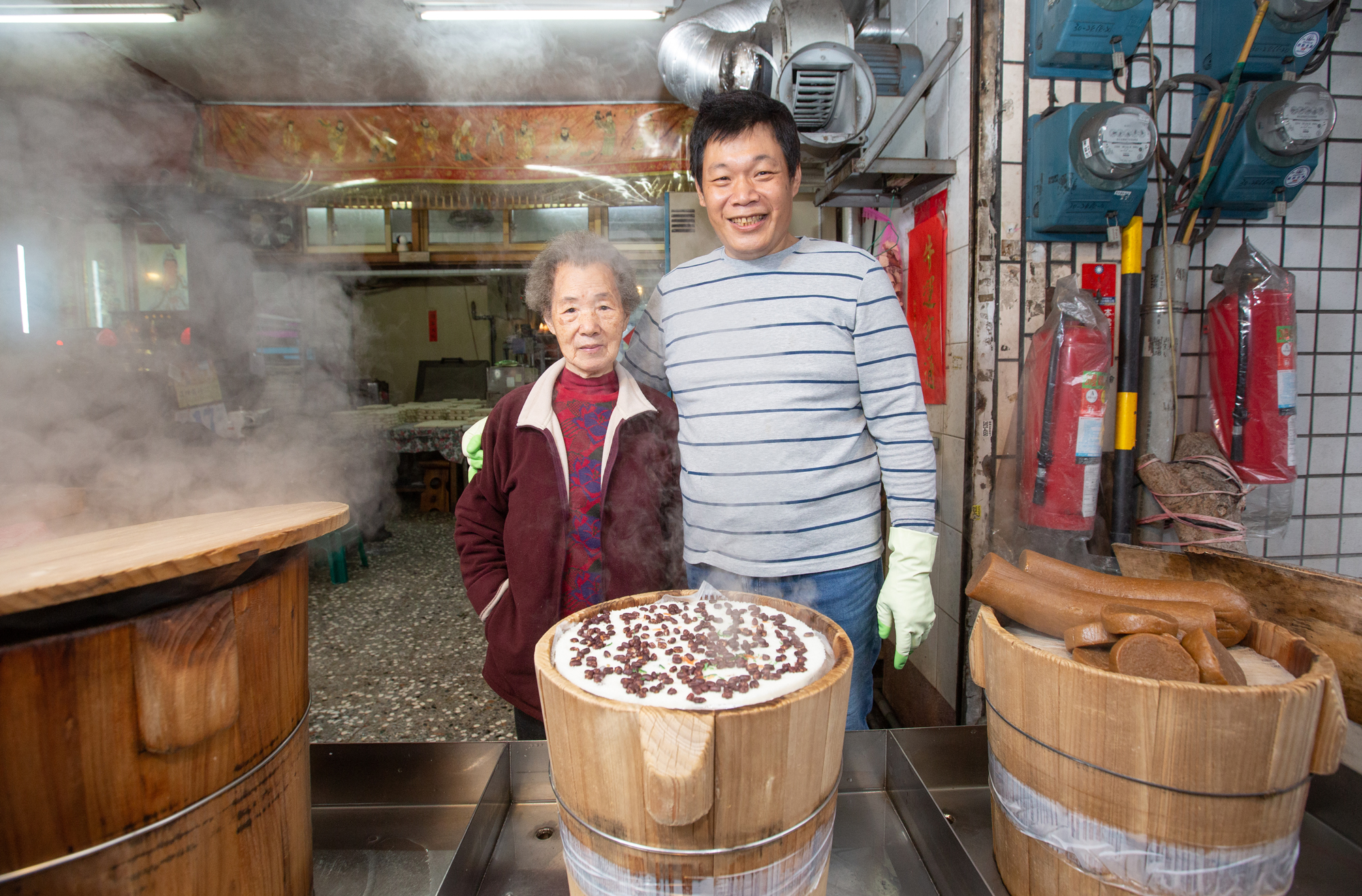 周翁領花（左）66年前從大陳島撤退來台，為了養家開店賣年糕，因為太辛苦，曾勸么兒周國良（右）別再做這一行。