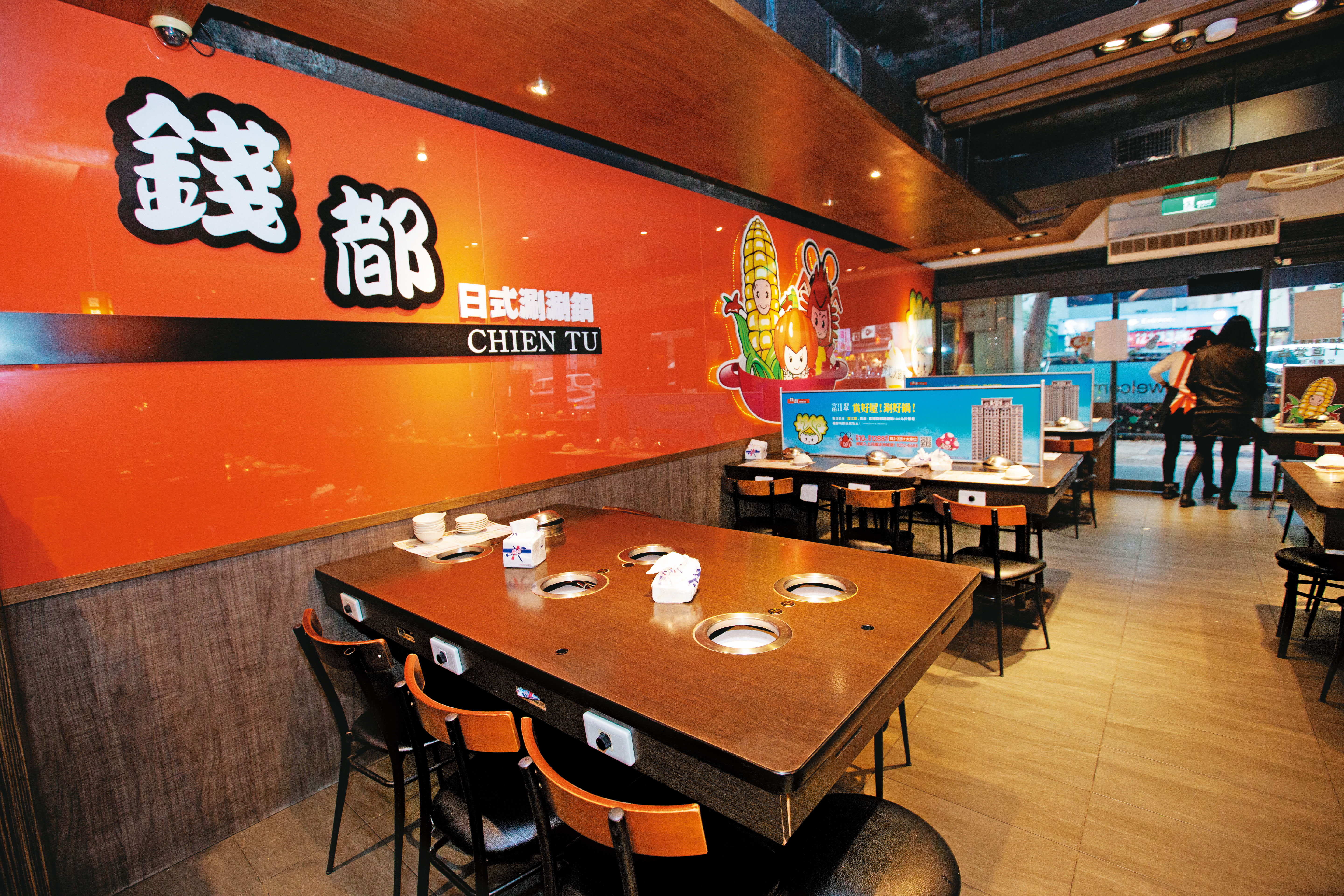 錢都一代店燈光較昏黃，桌子也以木質桌椅為主，裝潢看起來稍微簡單。
