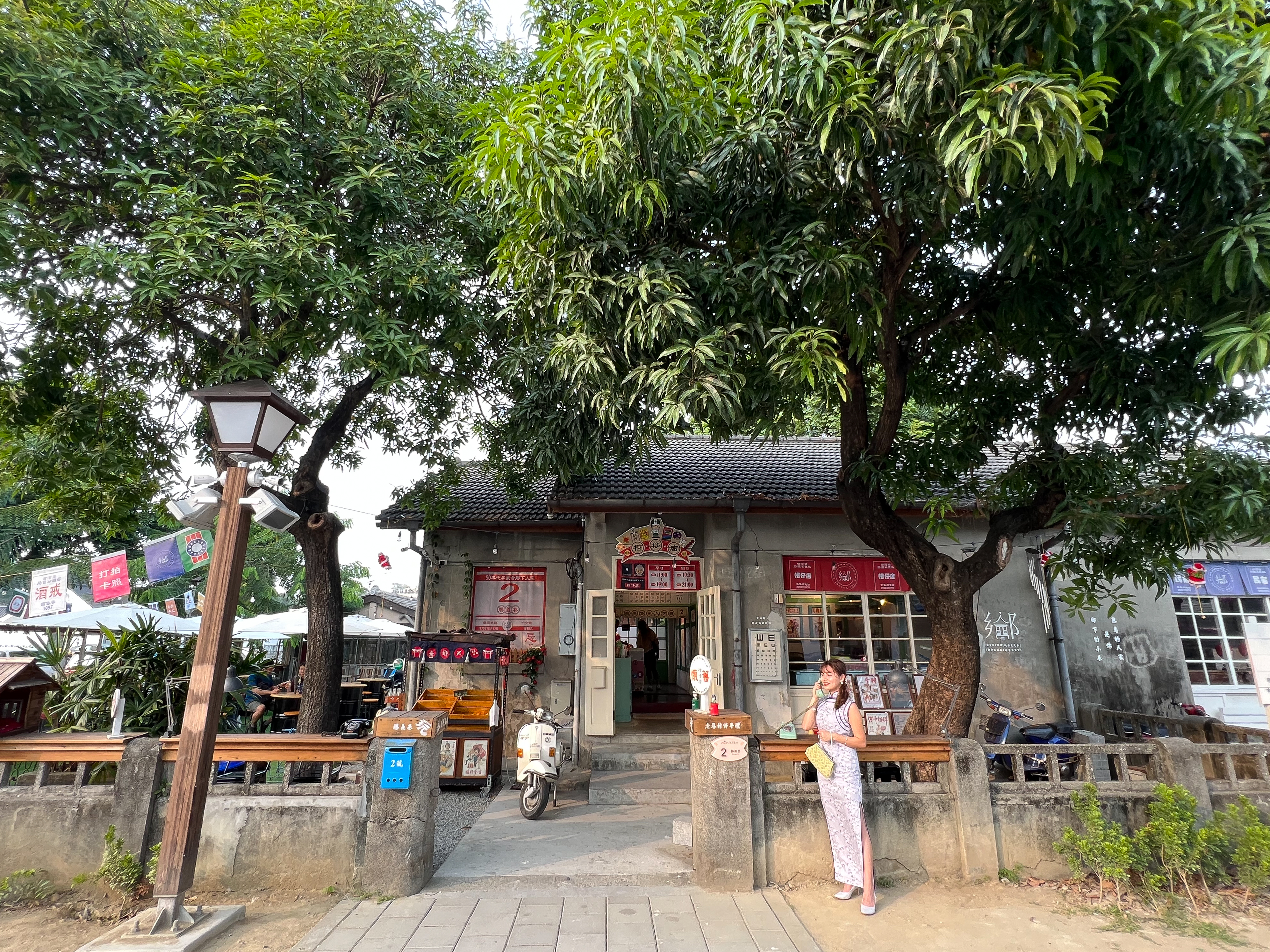 大樹下的「50年代屏東市鄉 下人家柑仔店」，外頭停放一輛瀟灑的偉士牌機車。 