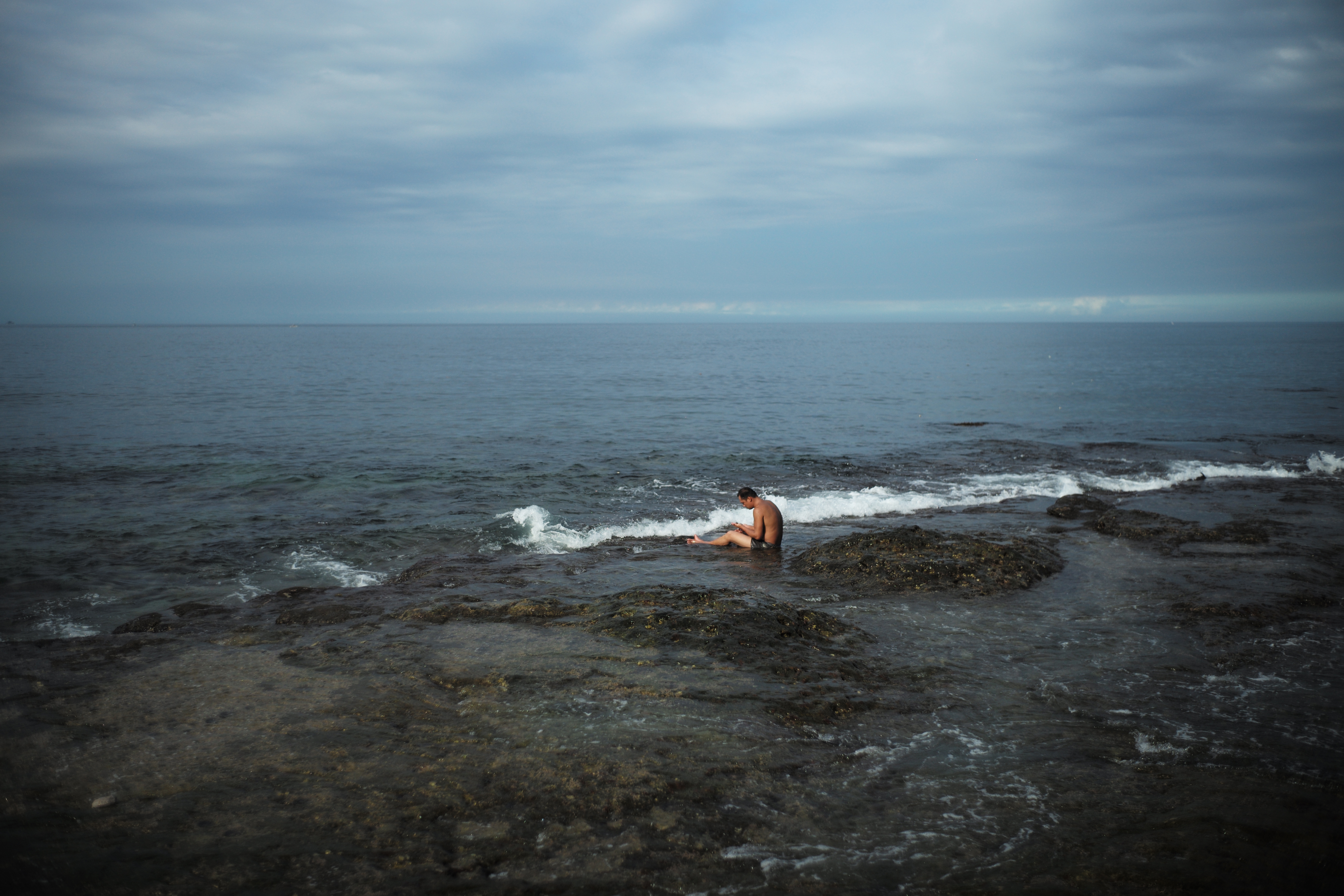 在平日午後的深澳海邊悠閒泡水的男人。