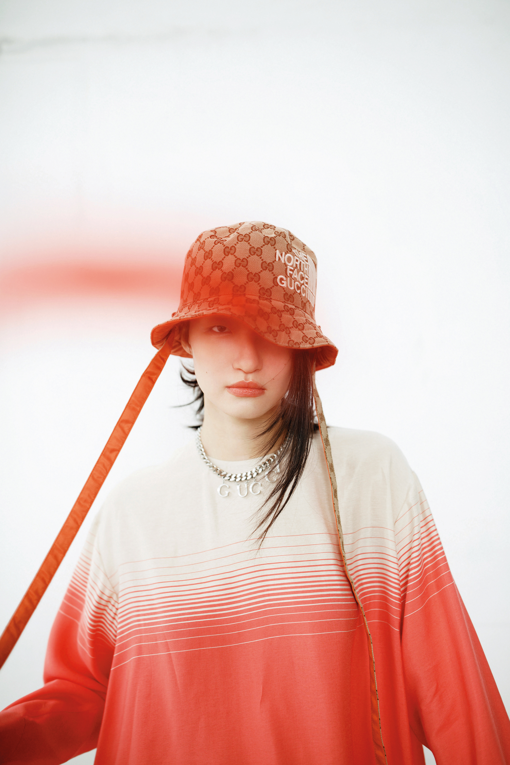 粉白漸層套衫 NT$20,800 by LONGCHAMP／雙面漁夫帽 NT$19,500 by GUCCI x The North Face／銀色手鍊作為項鍊 NT$26,700 by GUCCI