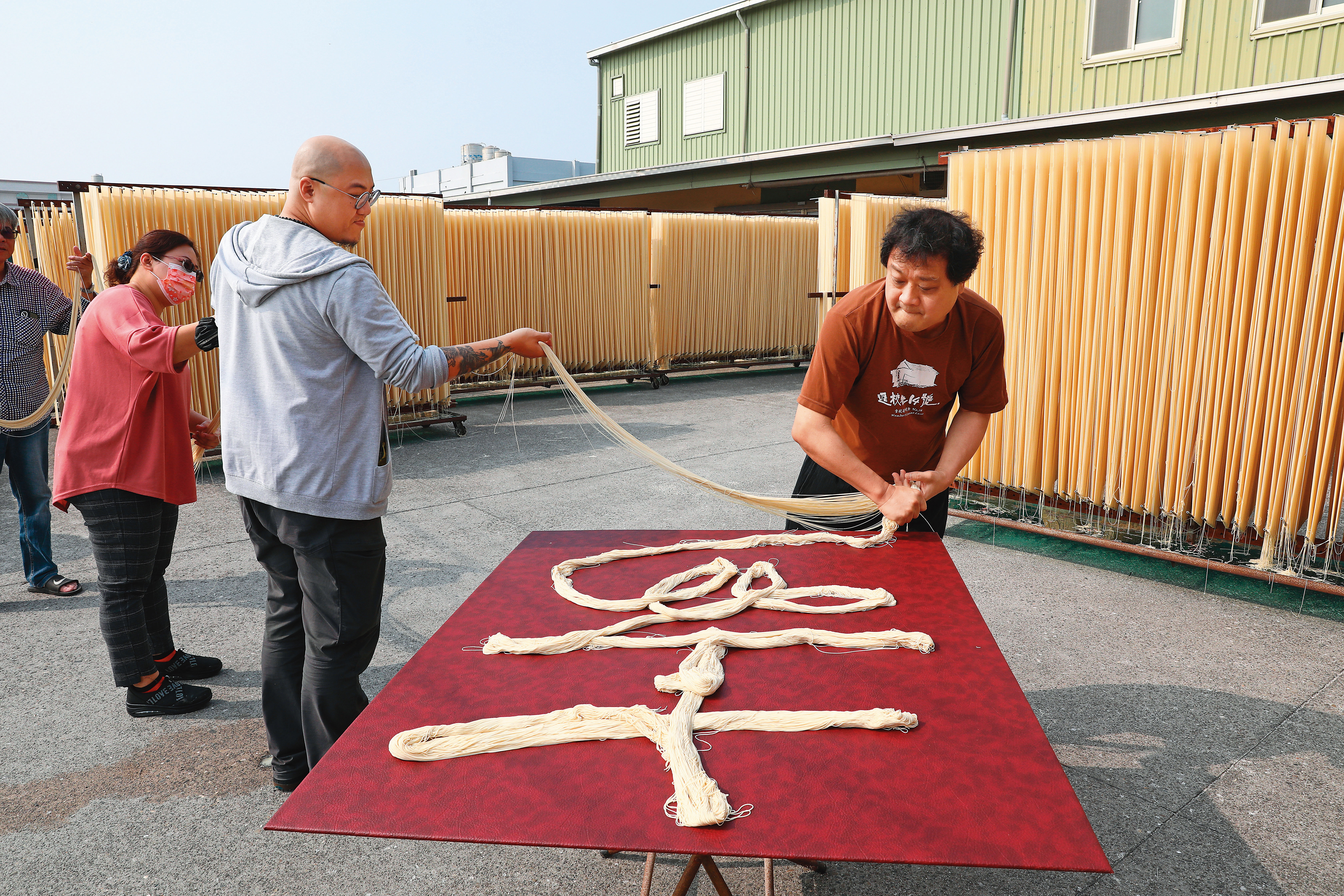 鄉親父老喜愛陳世憲(右)的作品。圖為陳世憲受邀至彰化麵線工廠,以麵線做複合媒材書法創作。