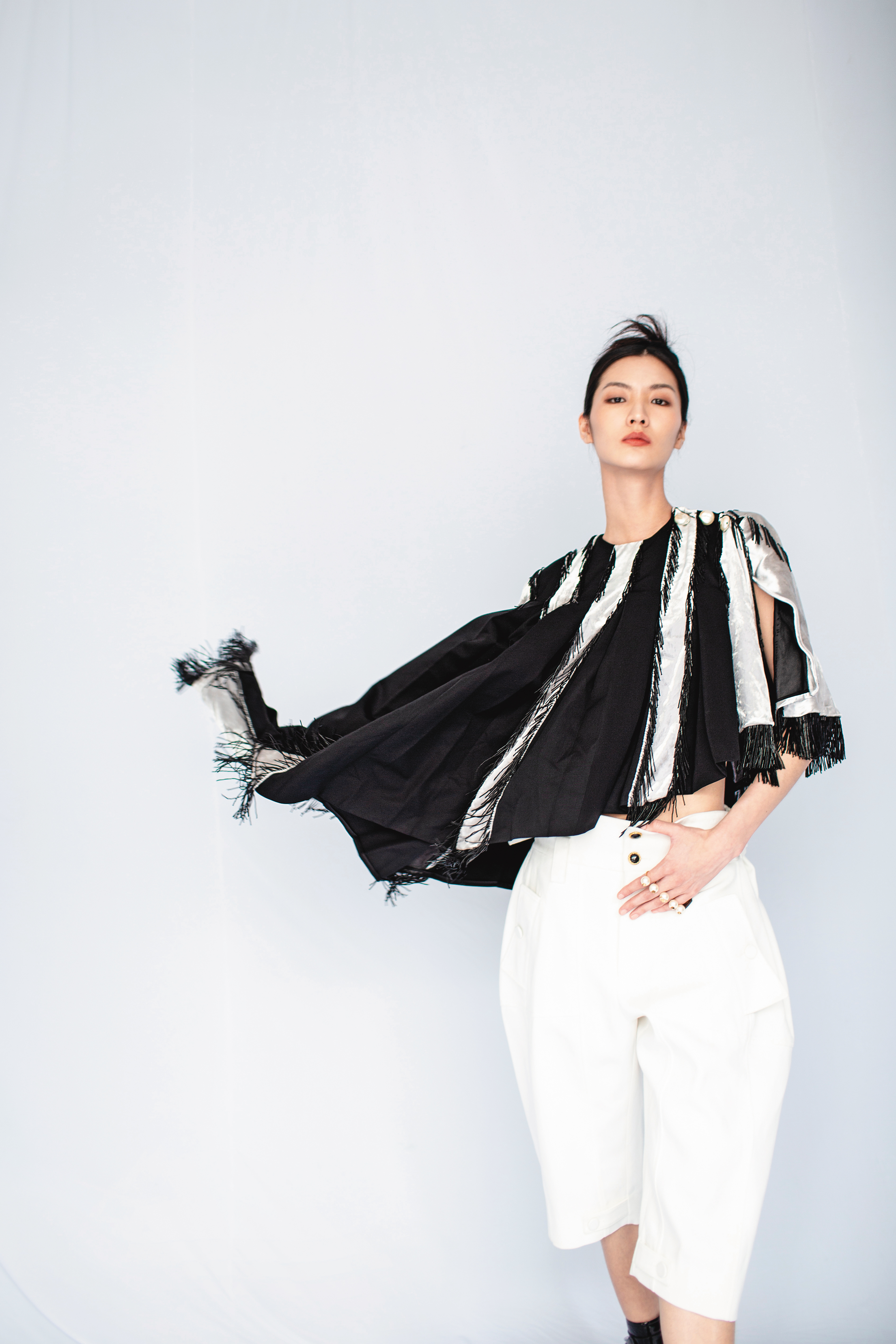 拼接斗篷NT$140,000 by LOUIS VUITTON；短版背心NT$9,700 by LOUIS VUITTON；寬版百慕達褲NT$21,700 by LOUIS VUITTON；珍珠指間戒，價格店洽 by VALENTINO GARAVANI。