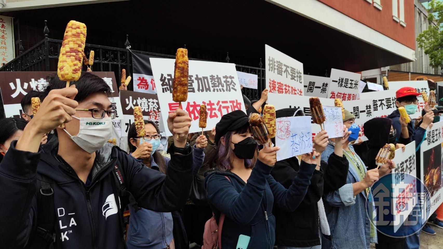 民眾手持烤玉米和水煮玉米比喻政府繼續販售紙菸，卻禁加熱菸。（讀者提供）