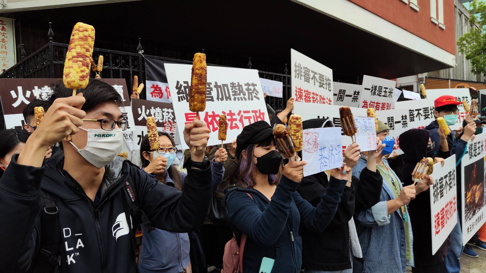 民眾手持烤玉米和水煮玉米比喻政府繼續販售紙菸,卻禁加熱菸。(讀者提供)
