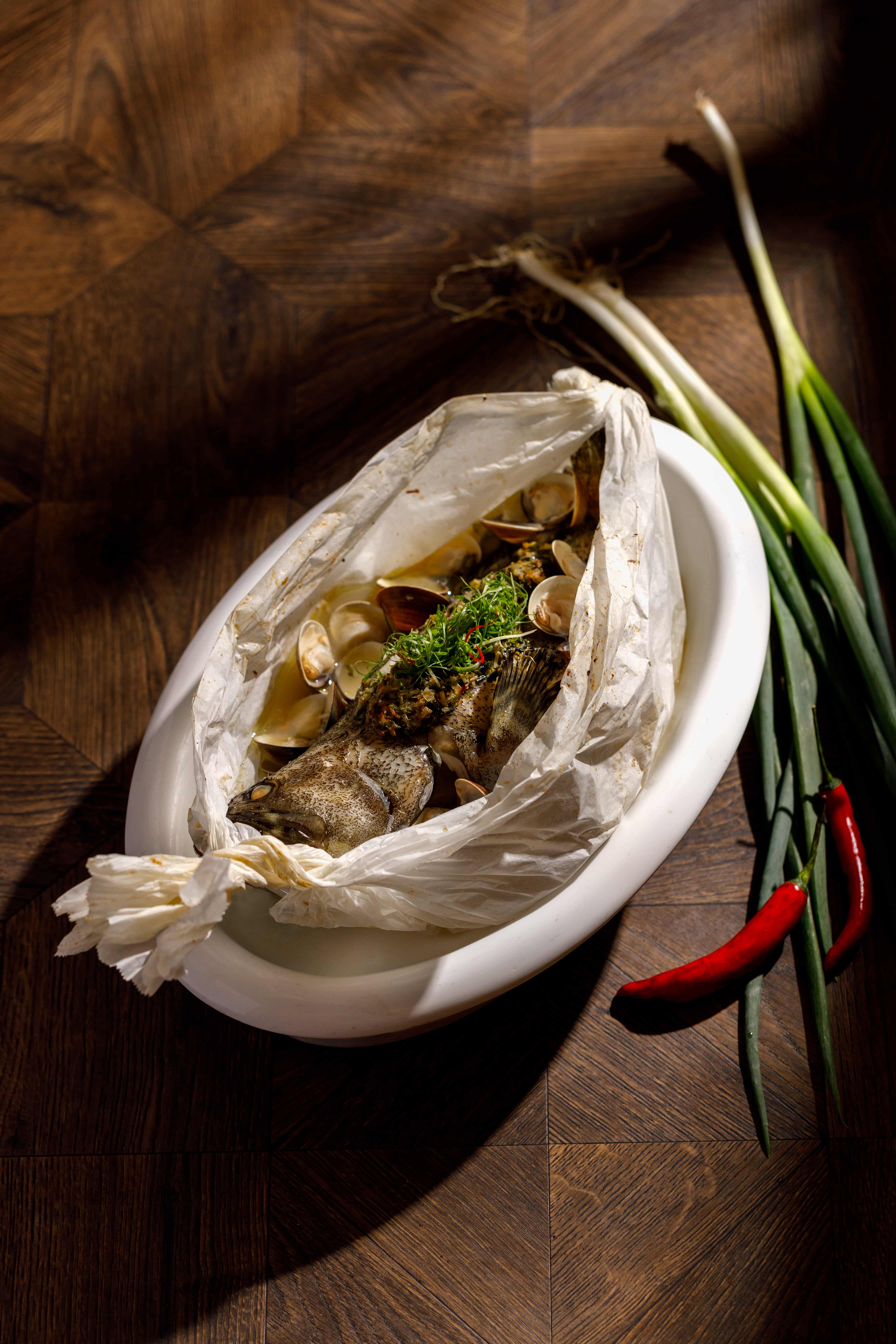 「鮮蛤紙包龍虎斑」打破過往桌菜的酒精 蒸魚盤形式，以歐式紙包魚手法出場。