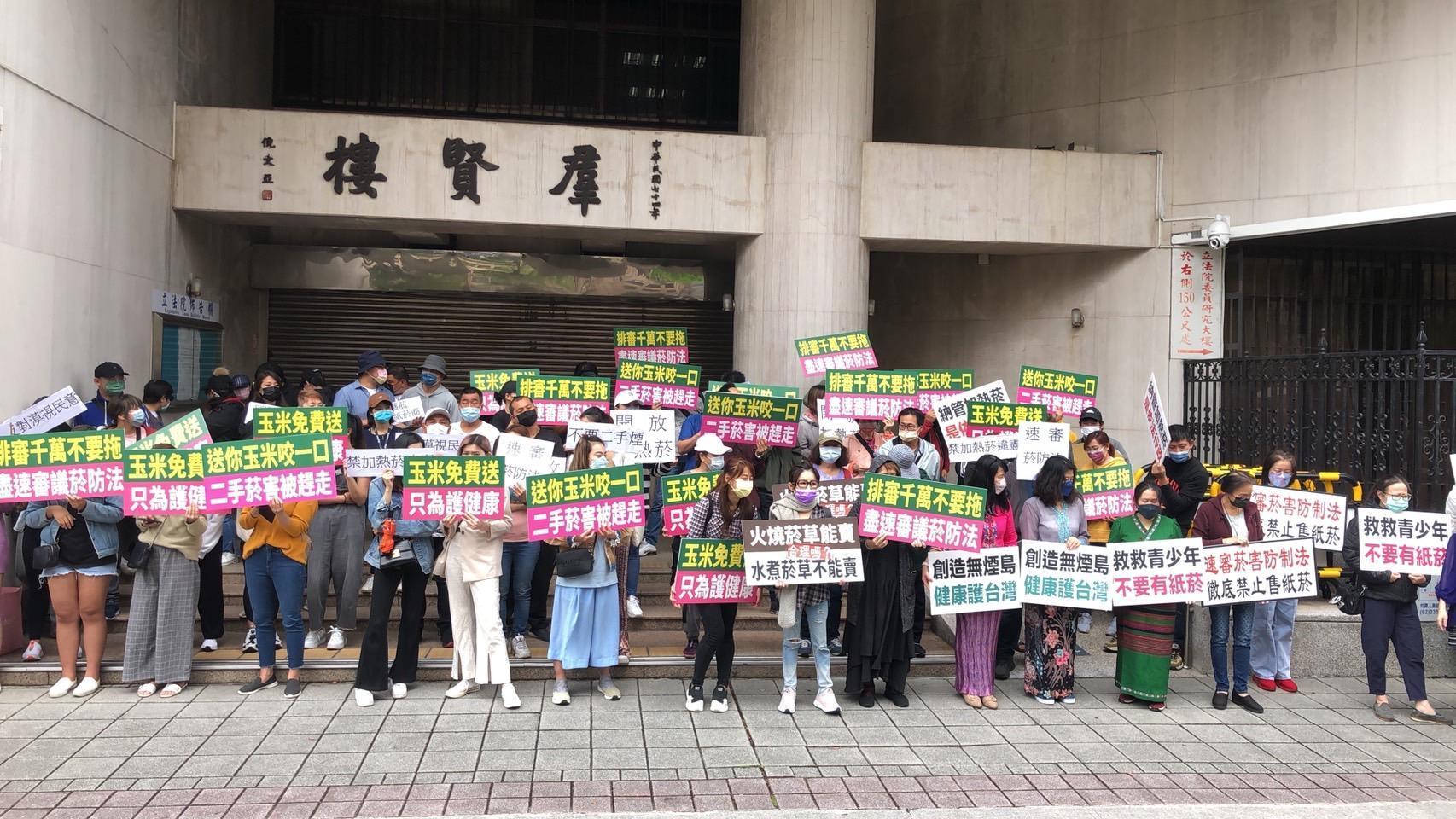 百名網友持標語前進立法院，嗆聲立委要求盡速排審《菸防法》。（讀者提供）