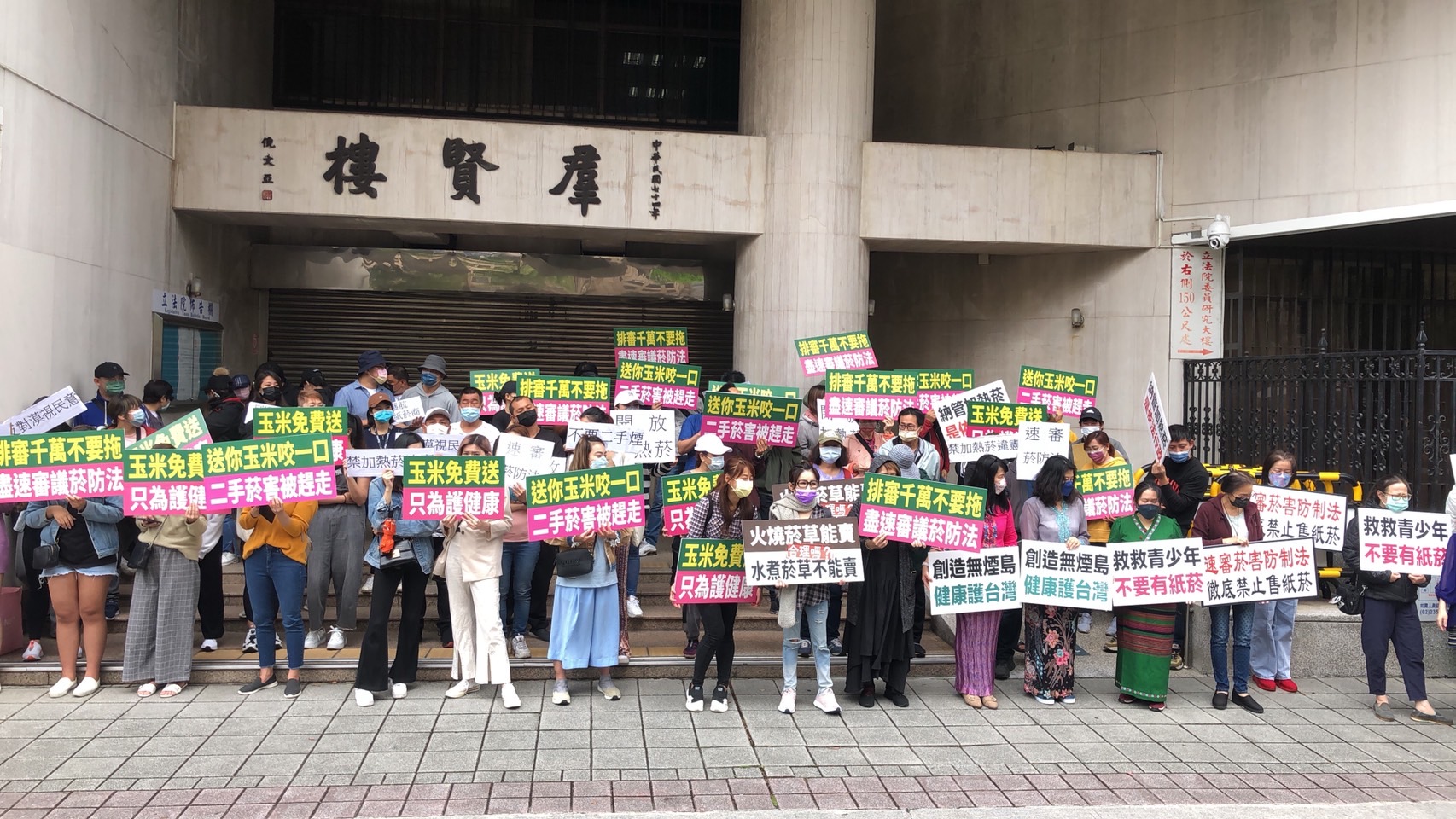 百名網友持標語前進立法院，嗆聲立委要求盡速排審《菸防法》。（讀者提供）