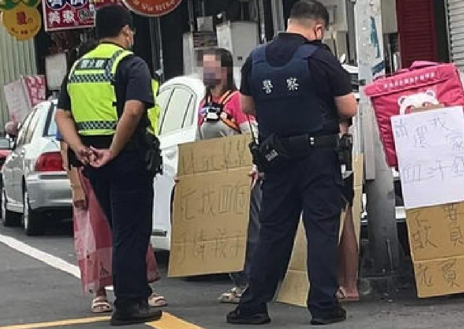 王女攜子在永康區永華路與永中街100巷口舉牌抗議，警方據報前往關心。（翻攝外送員的奇聞怪事）