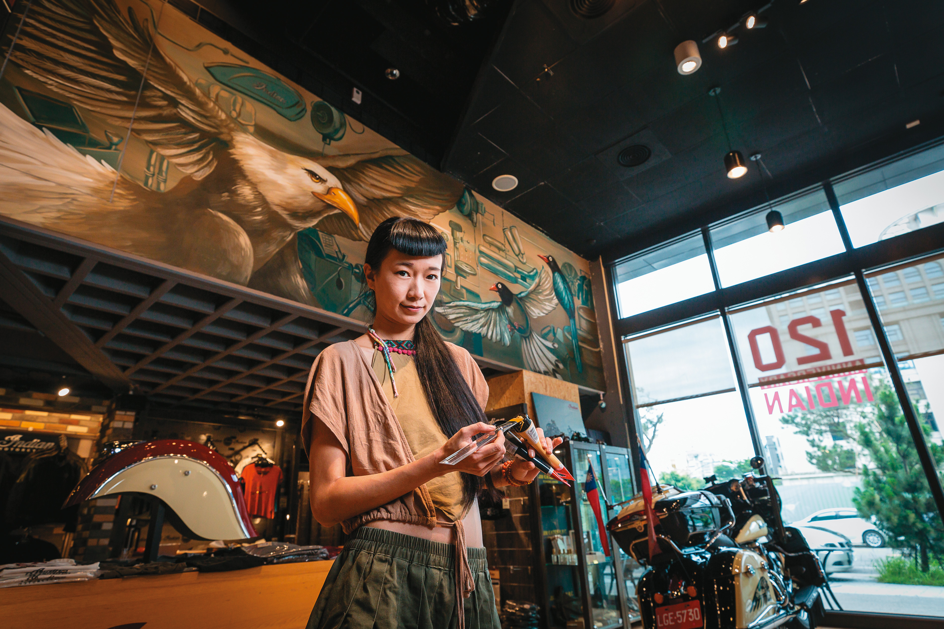 台藝大美術學系研究所碩士陳于安，不拘泥形式，是少數願意接案的藝術家。背後為她繪製的美國鷹與台灣藍鵲展翅對望壁畫。